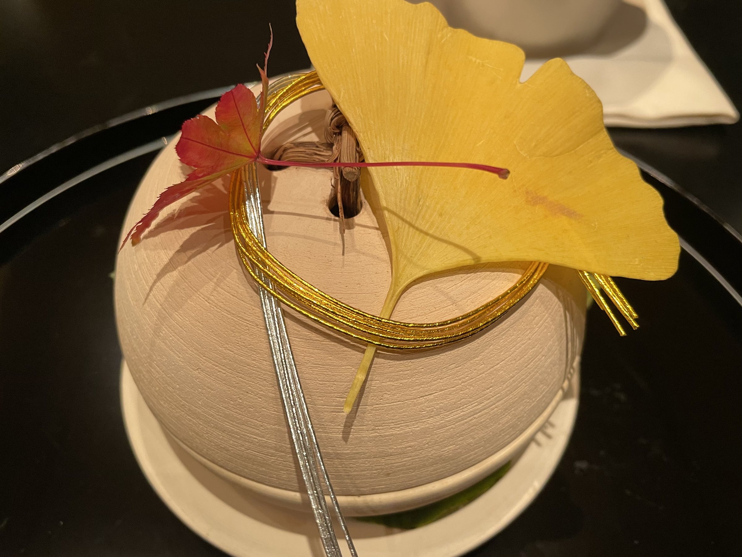 Maple and ginkgo leaves, tied with gold cord over a covered vessel.