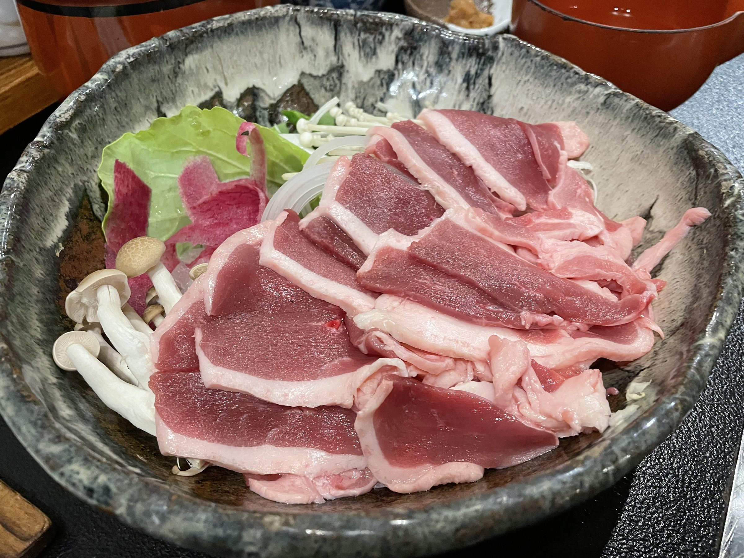 Slices of deep-red duck with mushrooms and leaves, ready for the pot.