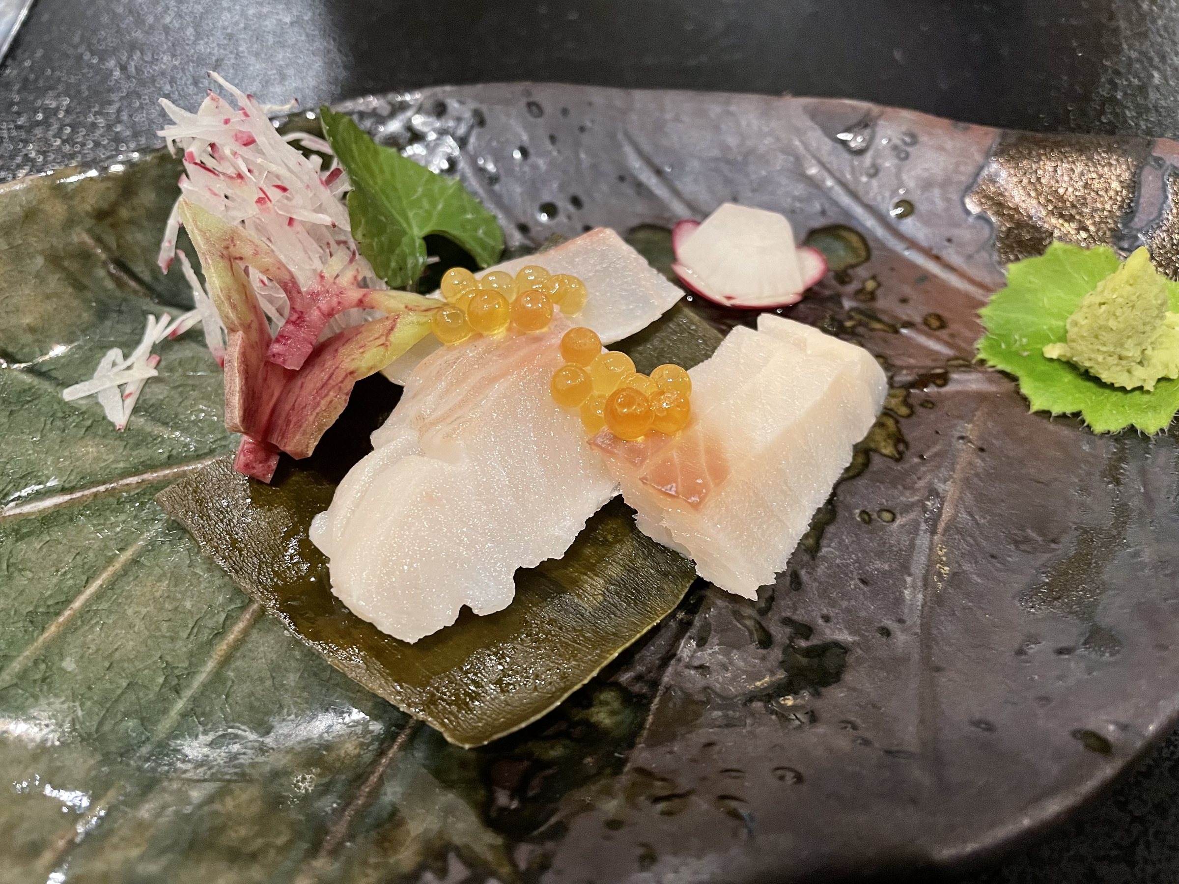 Sashimi with fruit garnish, served on a leaf-shaped ceramic plate.