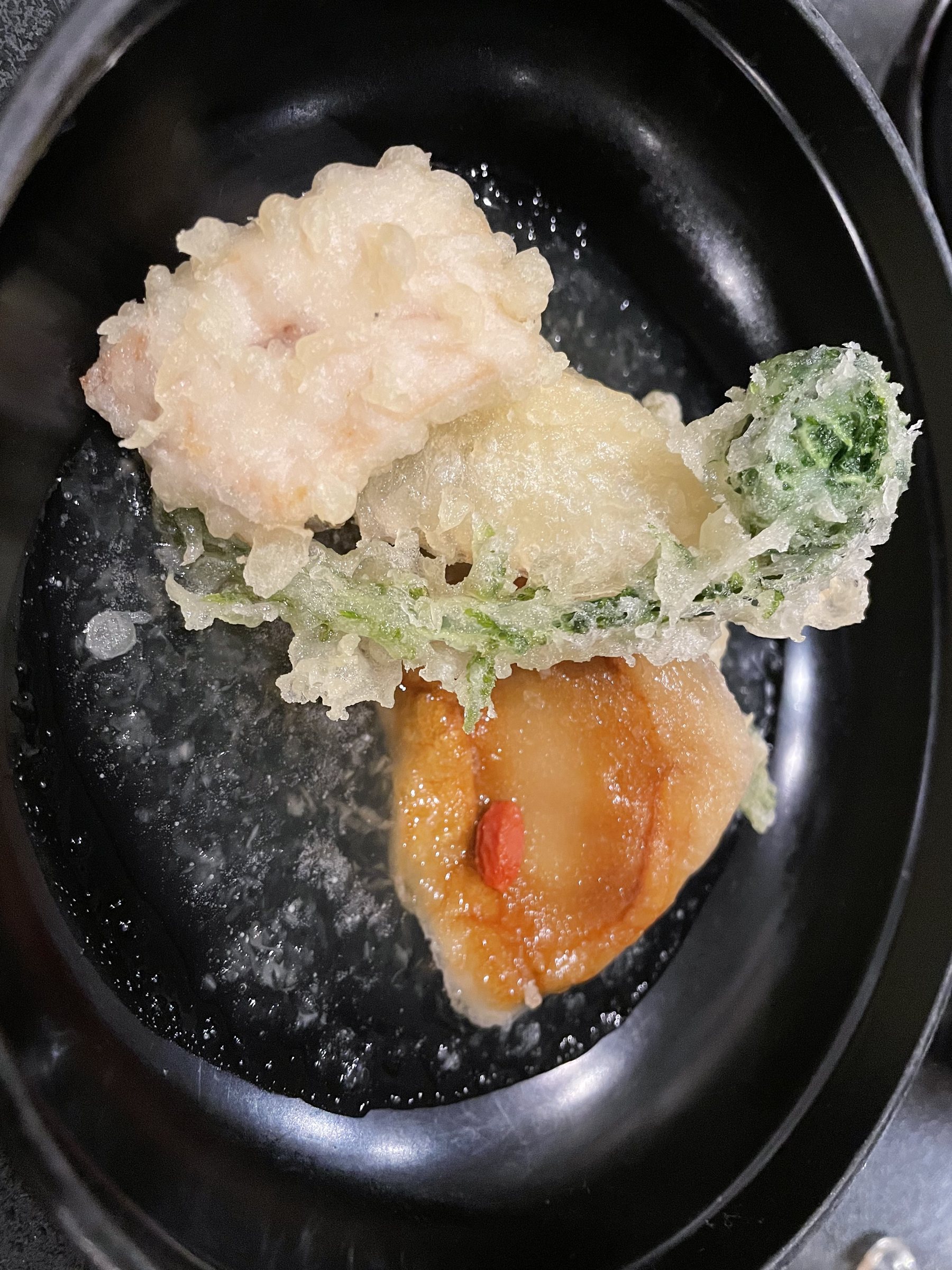 Tempura of greens and other pieces in a black lacquer dish.
