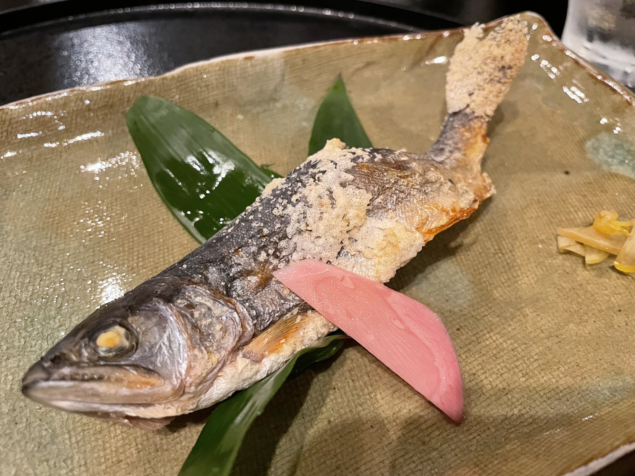A whole salt-grilled char on bamboo leaves, its tail crusted with salt.