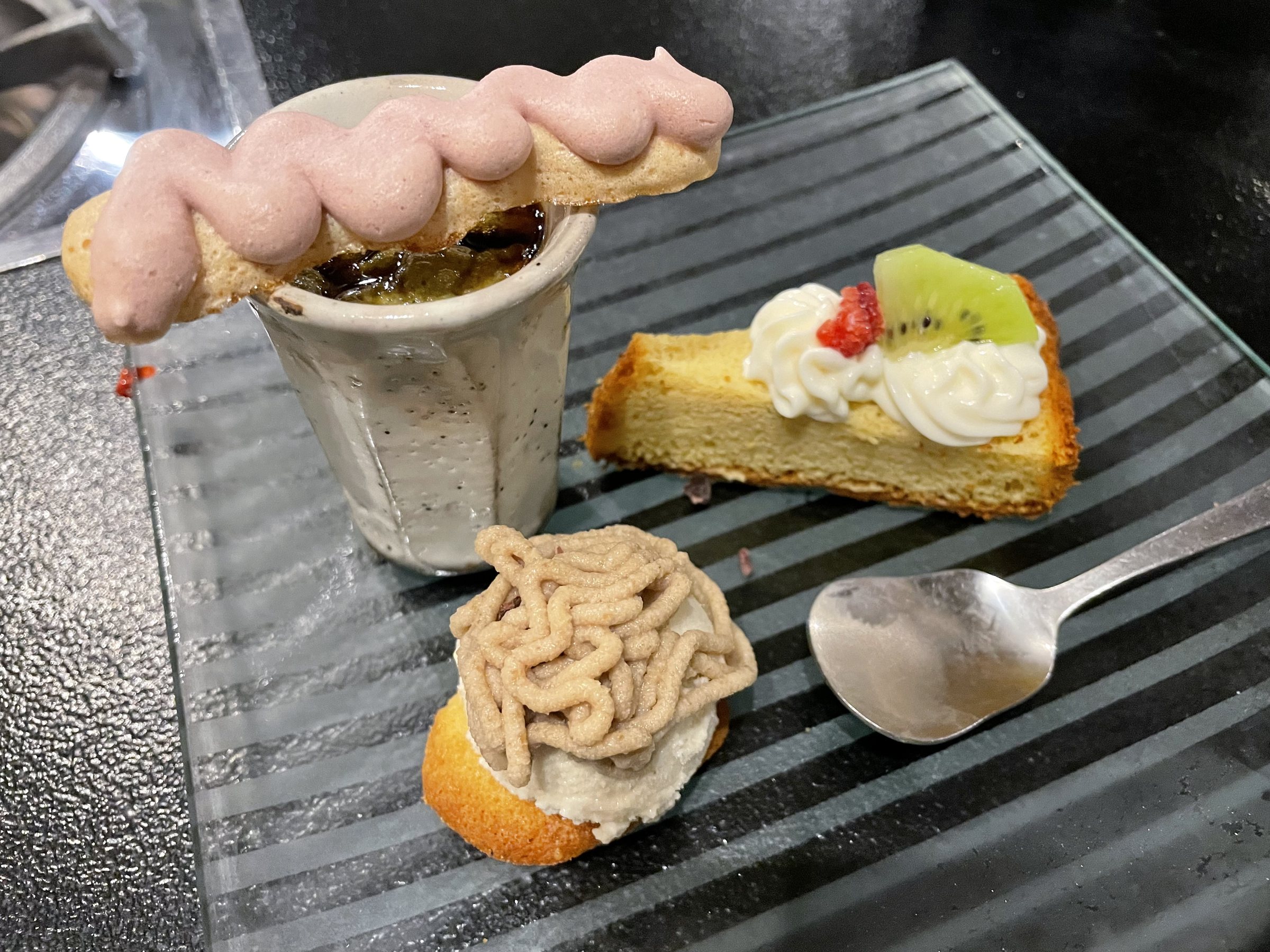 Three gluten-free desserts on a striped glass plate, among them a chestnut-cream cake and a sponge topped with cream and kiwi.
