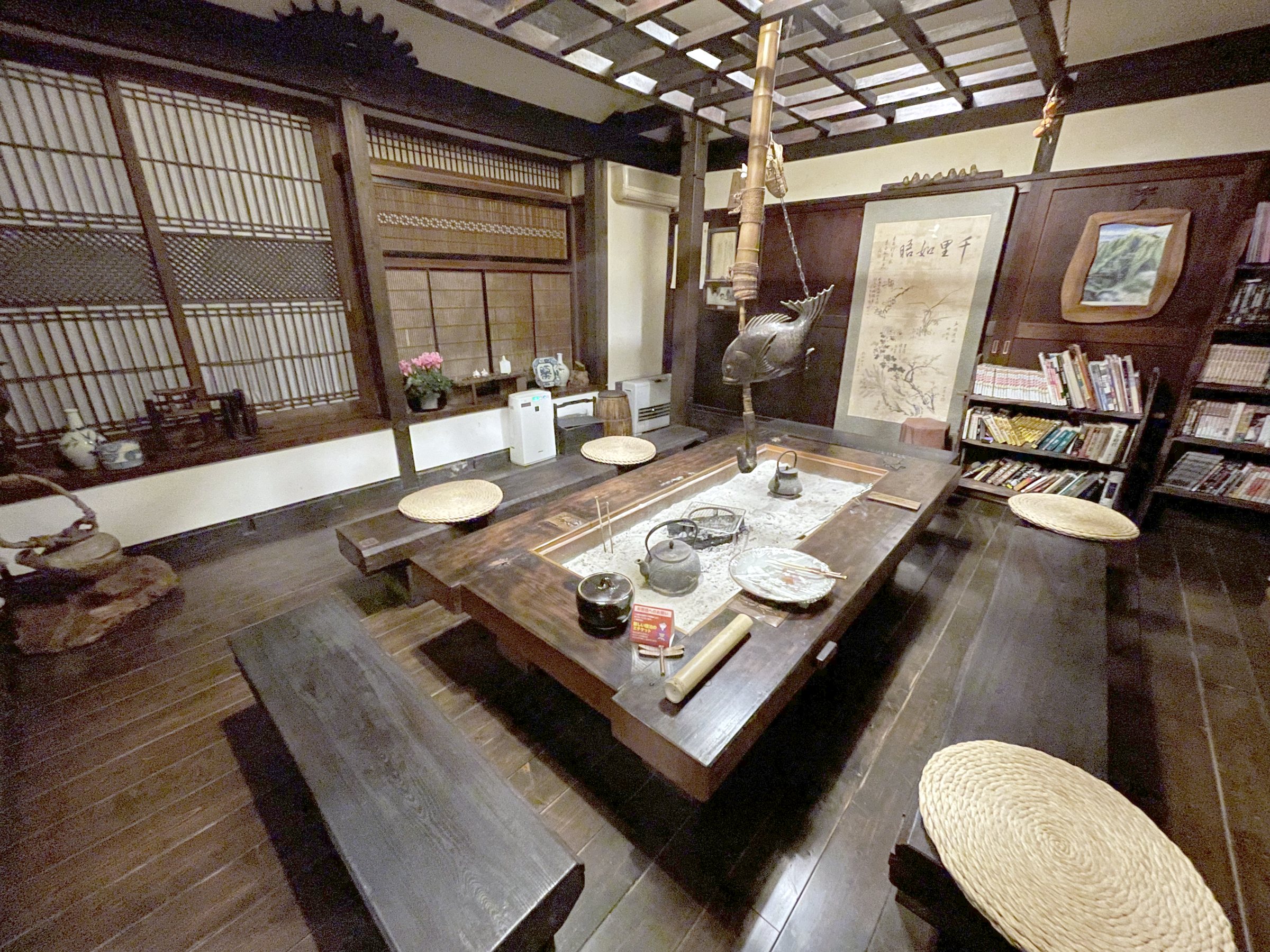 A lounge with a sunken hearth table, wooden benches and shelves of books.
