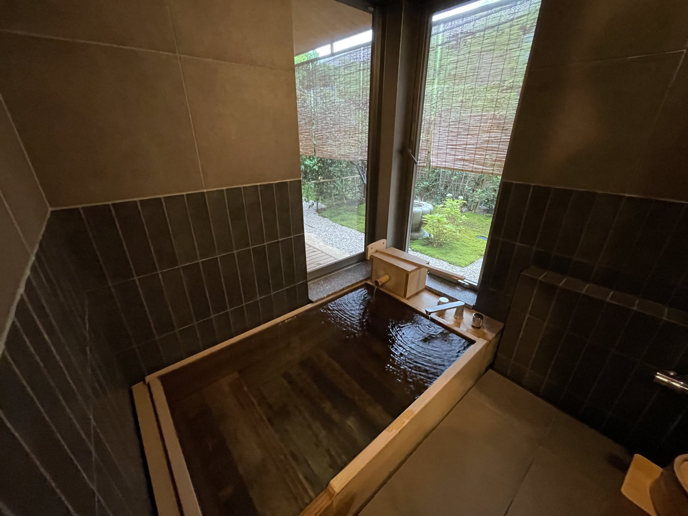 The room’s semi-open-air bath: a wooden tub by a window onto greenery.