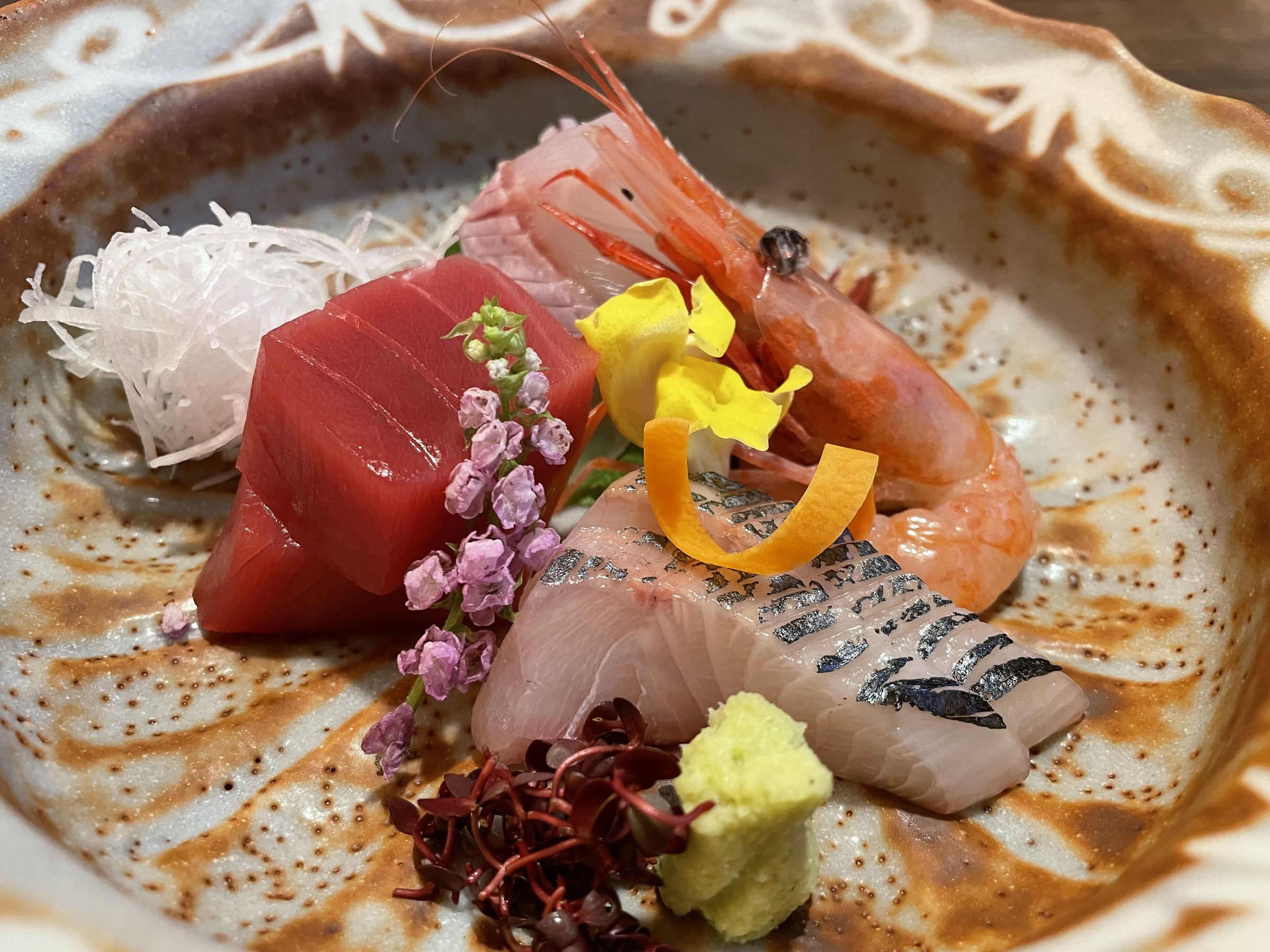 Sashimi of tuna, sweet shrimp and white fish, with edible flowers and wasabi.