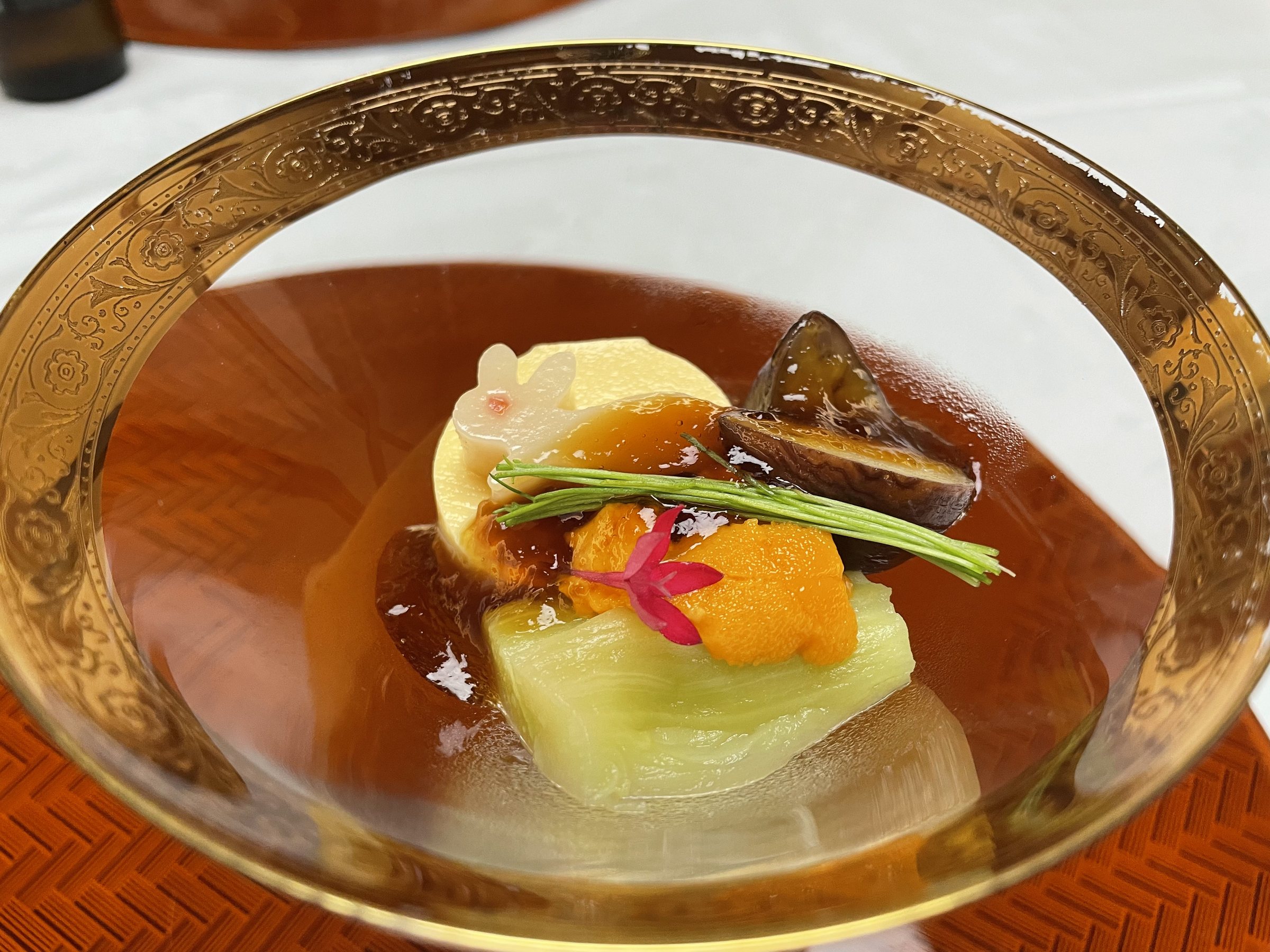 The appetiser in a gold-rimmed glass bowl, topped with sea urchin and leek shoots.