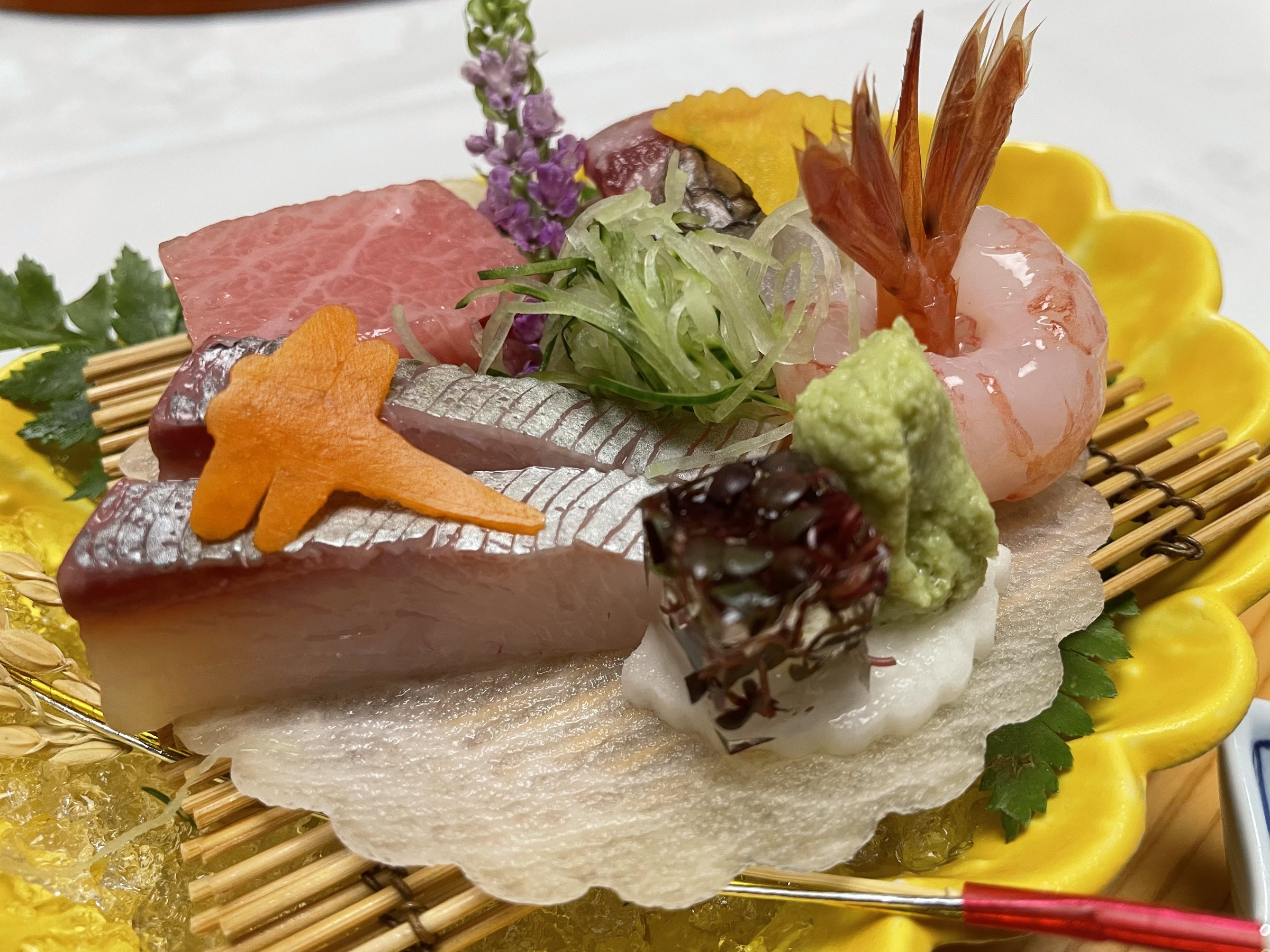 The sashimi platter up close, on a bamboo mat over a yellow dish.