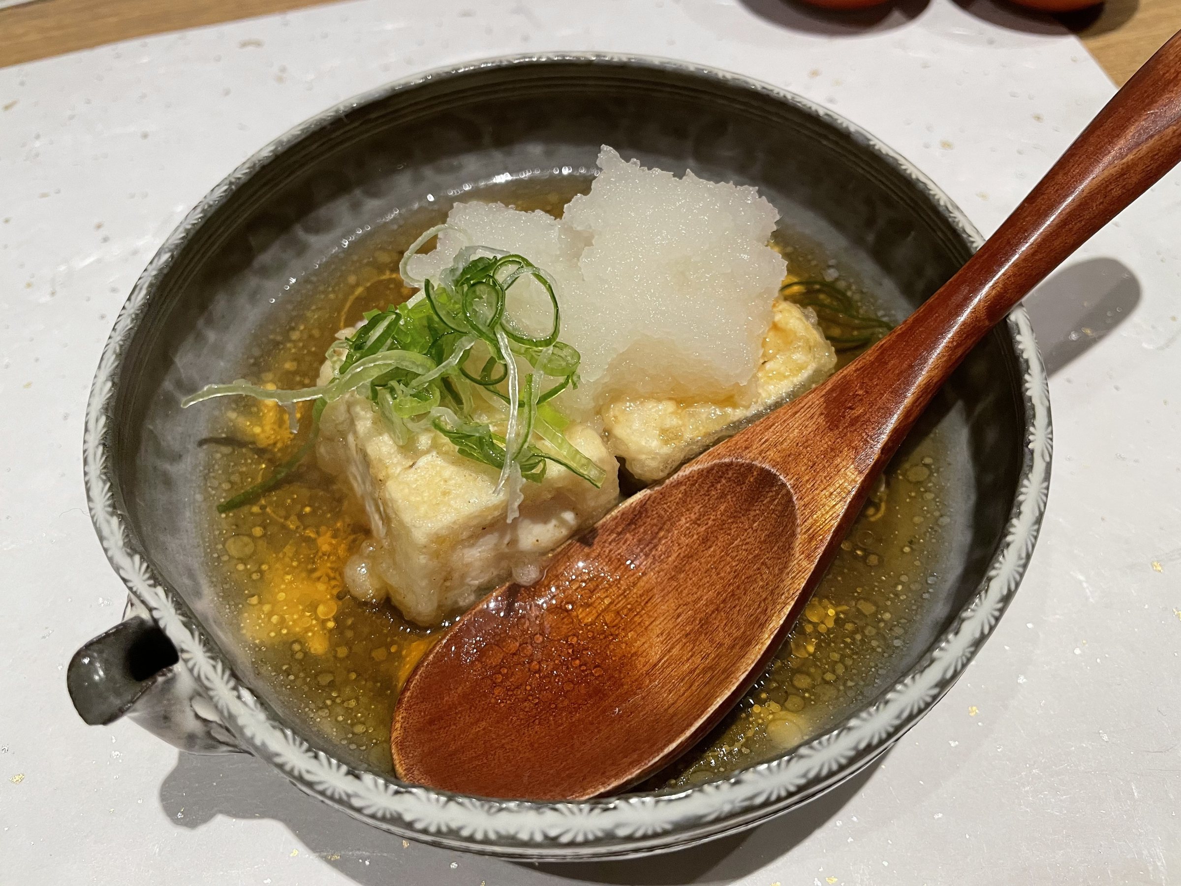 Fried tofu in broth with grated daikon and spring onion, served with a wooden spoon.