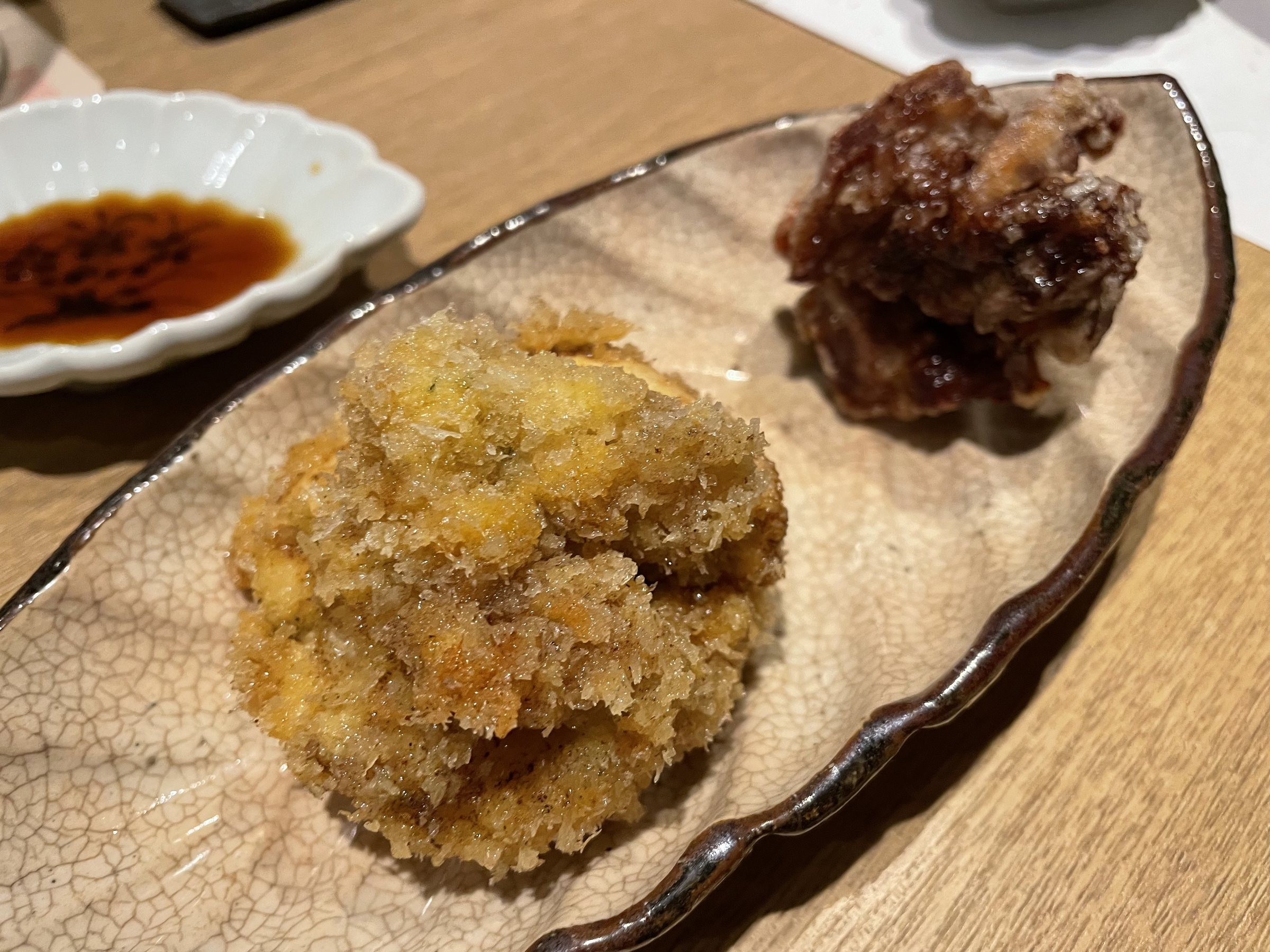 Two fried morsels, one in crisp breadcrumbs, with soy sauce for dipping.