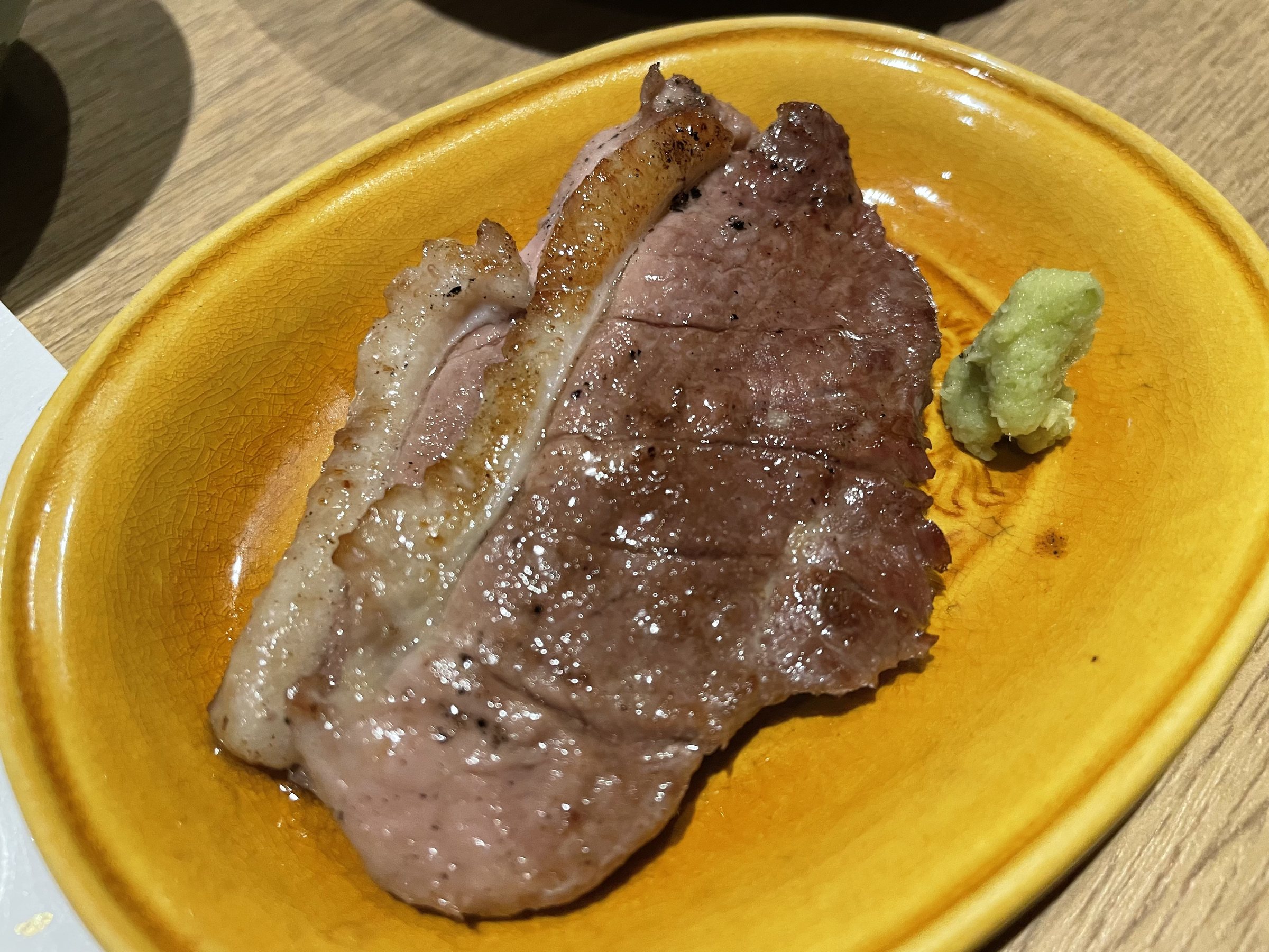 Slices of grilled meat with wasabi on a yellow plate.