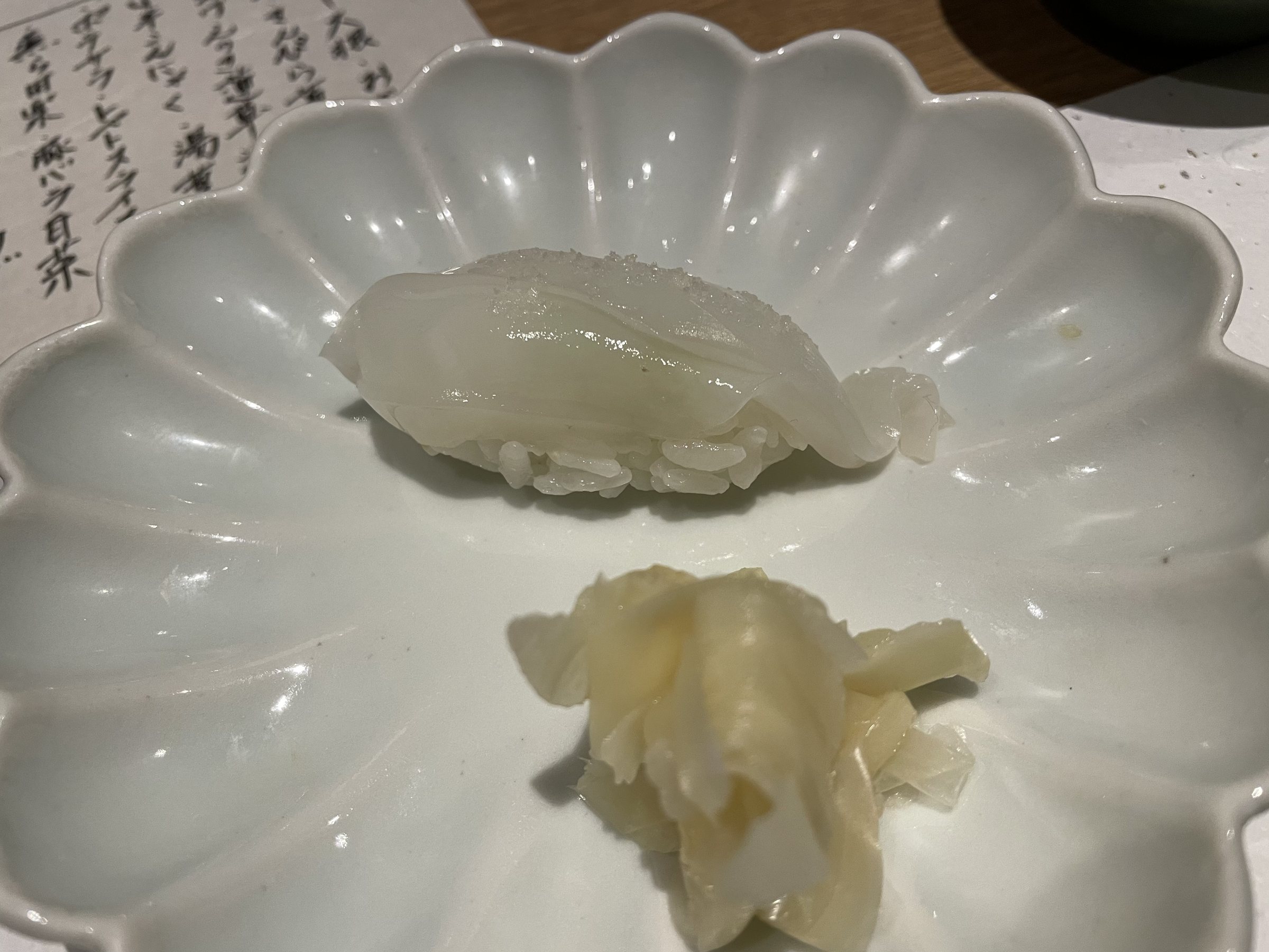 A translucent white nigiri, finely scored, with pickled ginger.