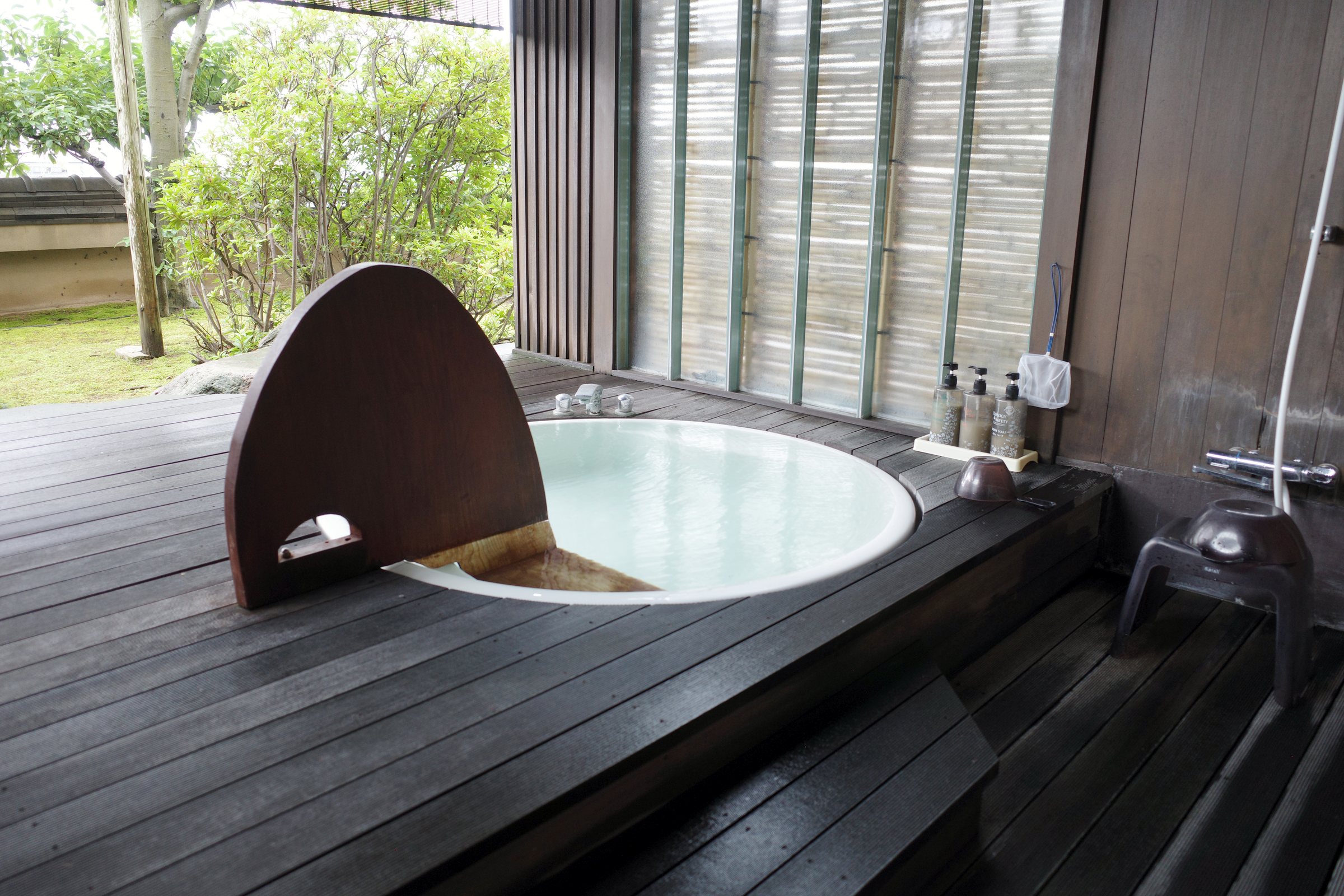 The private open-air bath: a round tub on a dark wooden deck, with pines beyond.