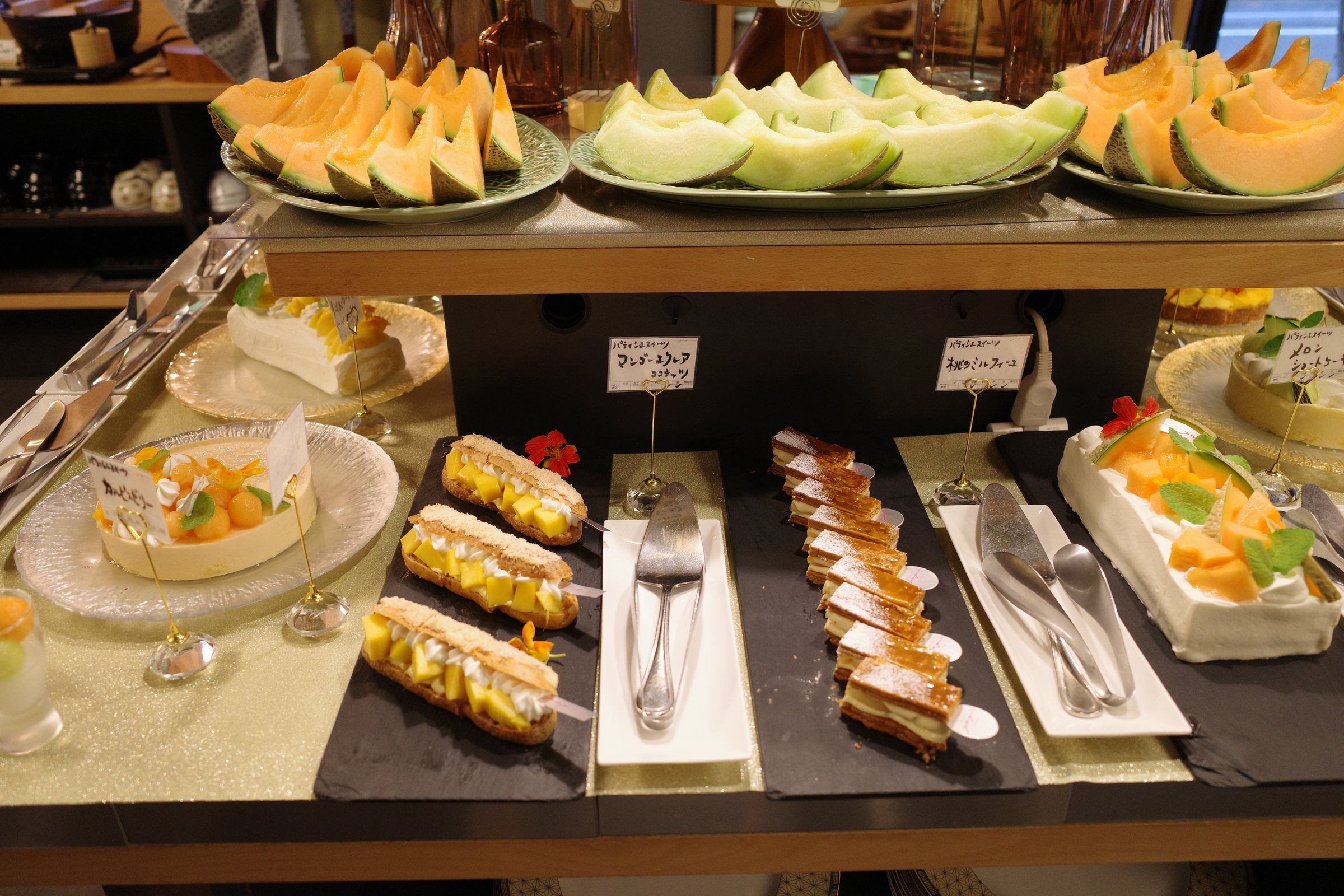 The dessert table, with slices of orange- and green-fleshed melon above rows of cakes.