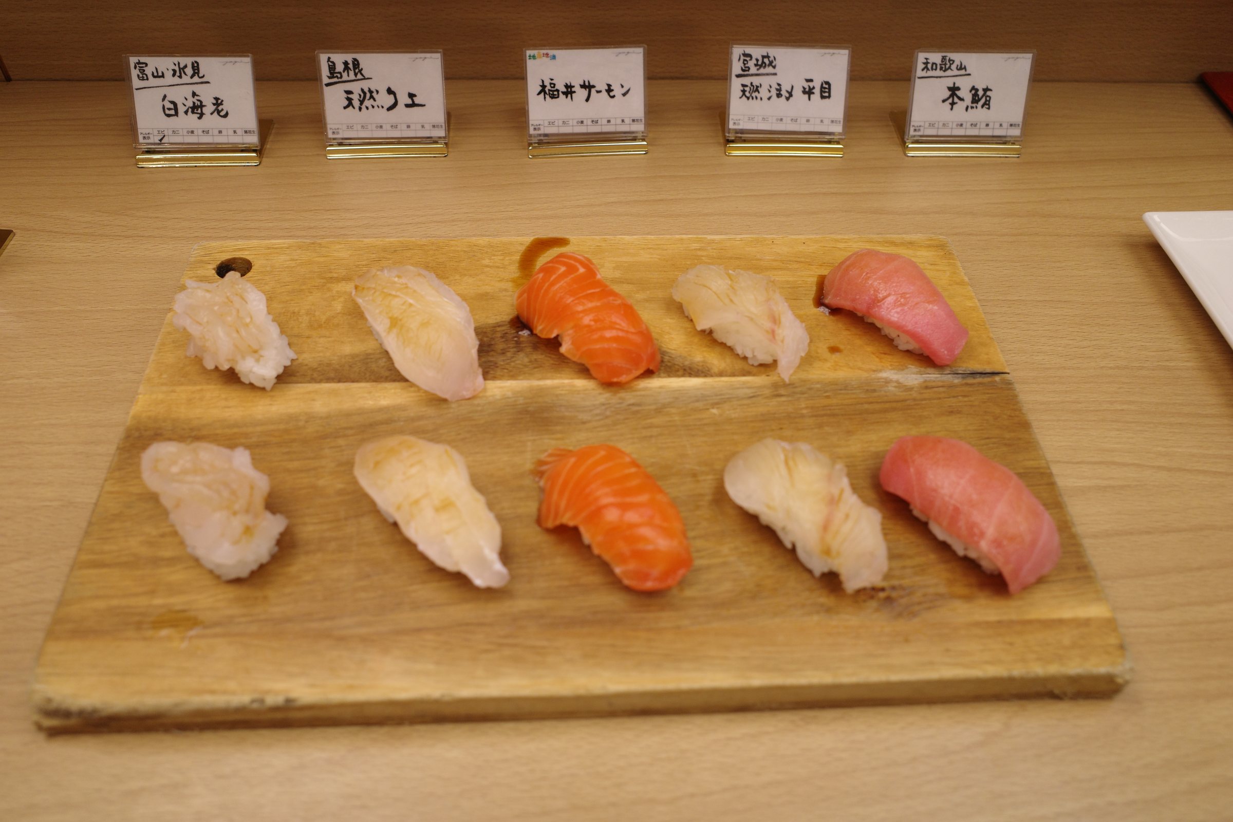 Nigiri sushi on a wooden board, each topping labeled.
