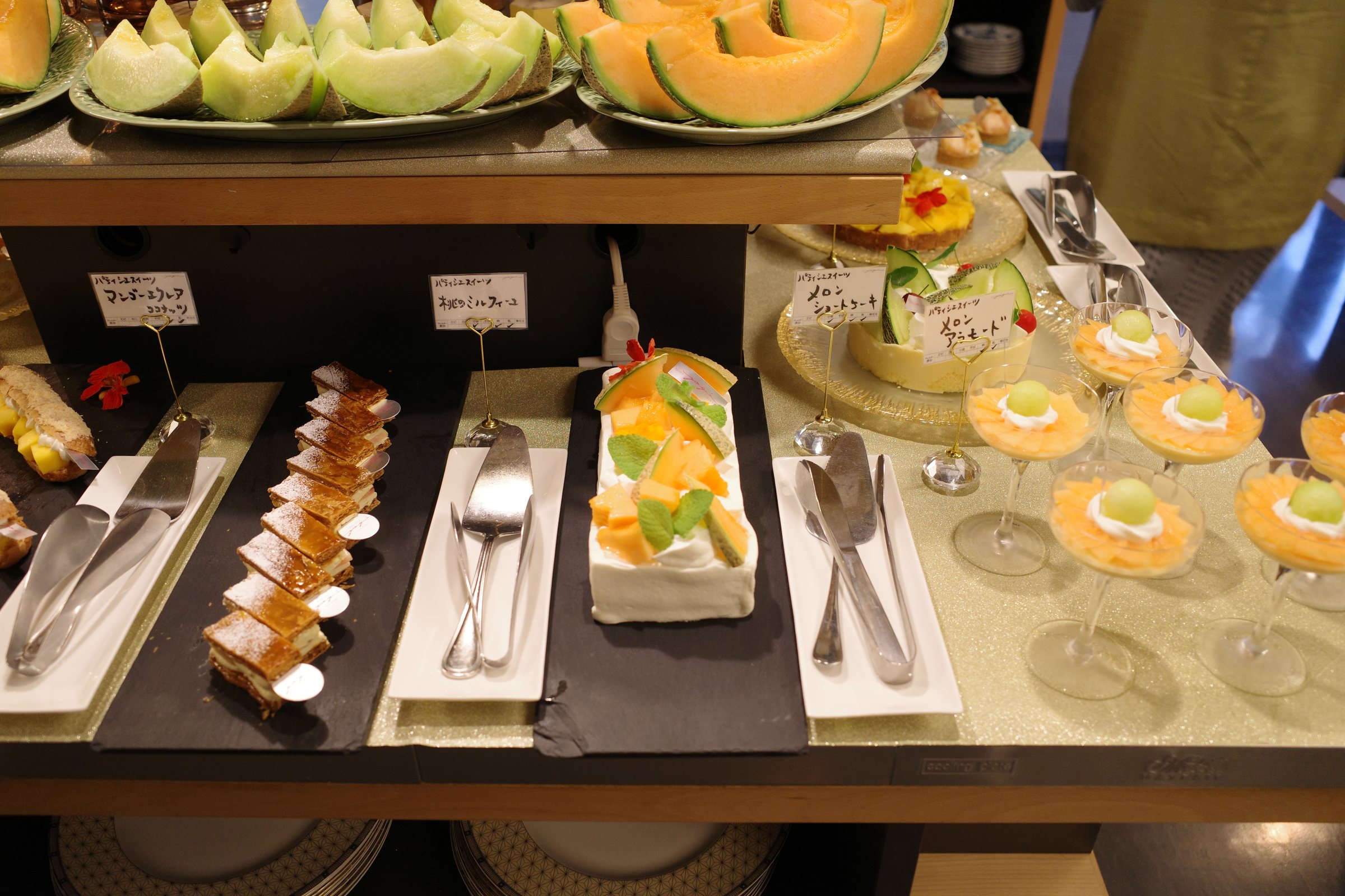 Rows of cakes, tarts and verrines beneath the melon display.