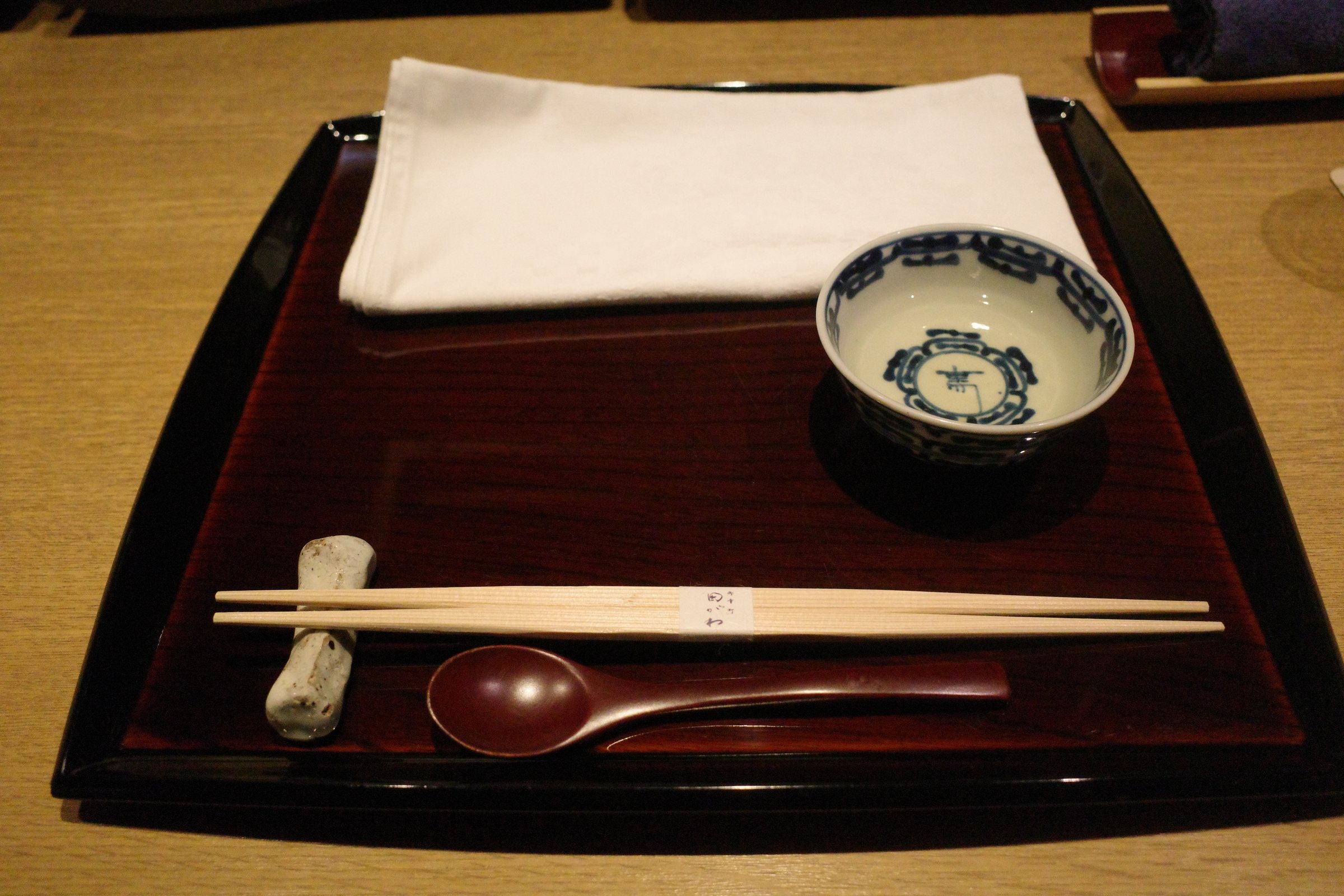 A place setting at the counter: a lacquered tray, napkin and chopsticks.