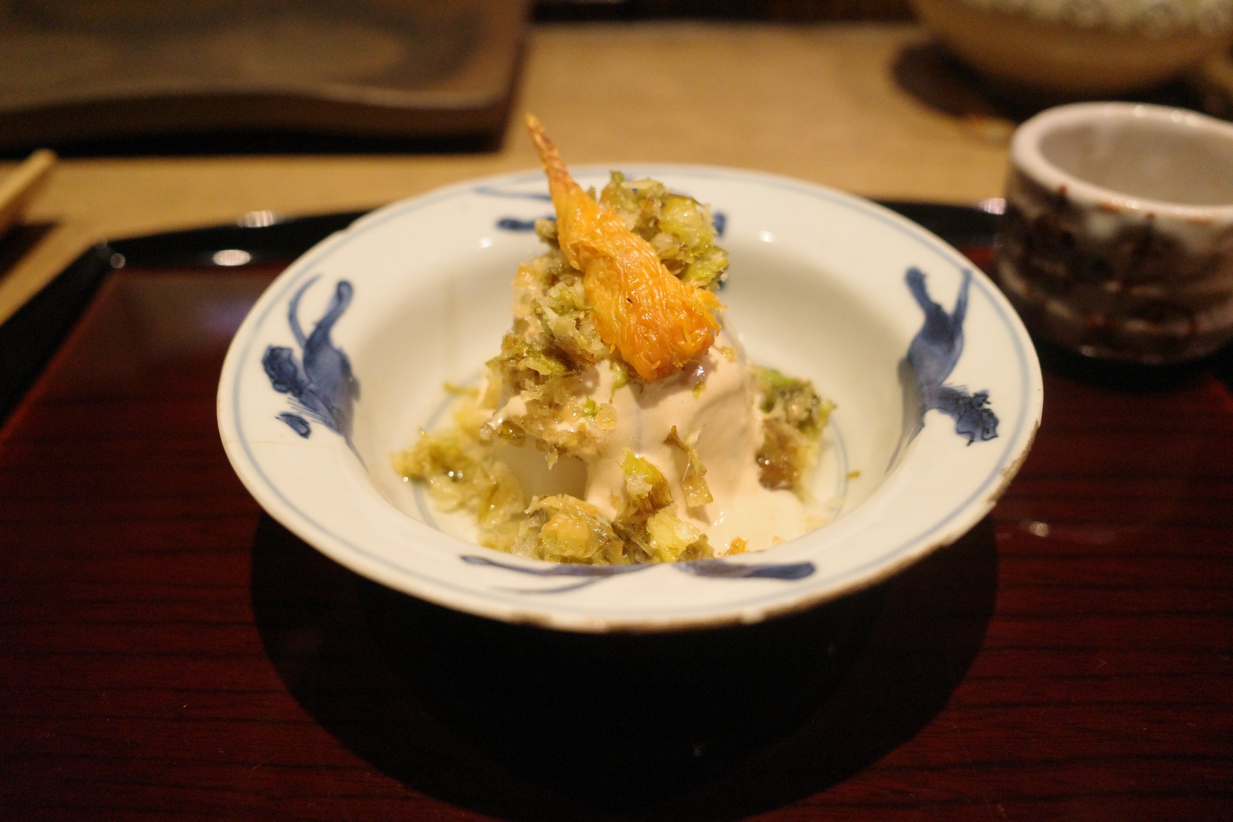 Simmered turnip scattered with crumbs of fried butterbur shoot and topped with a piece of bachiko.
