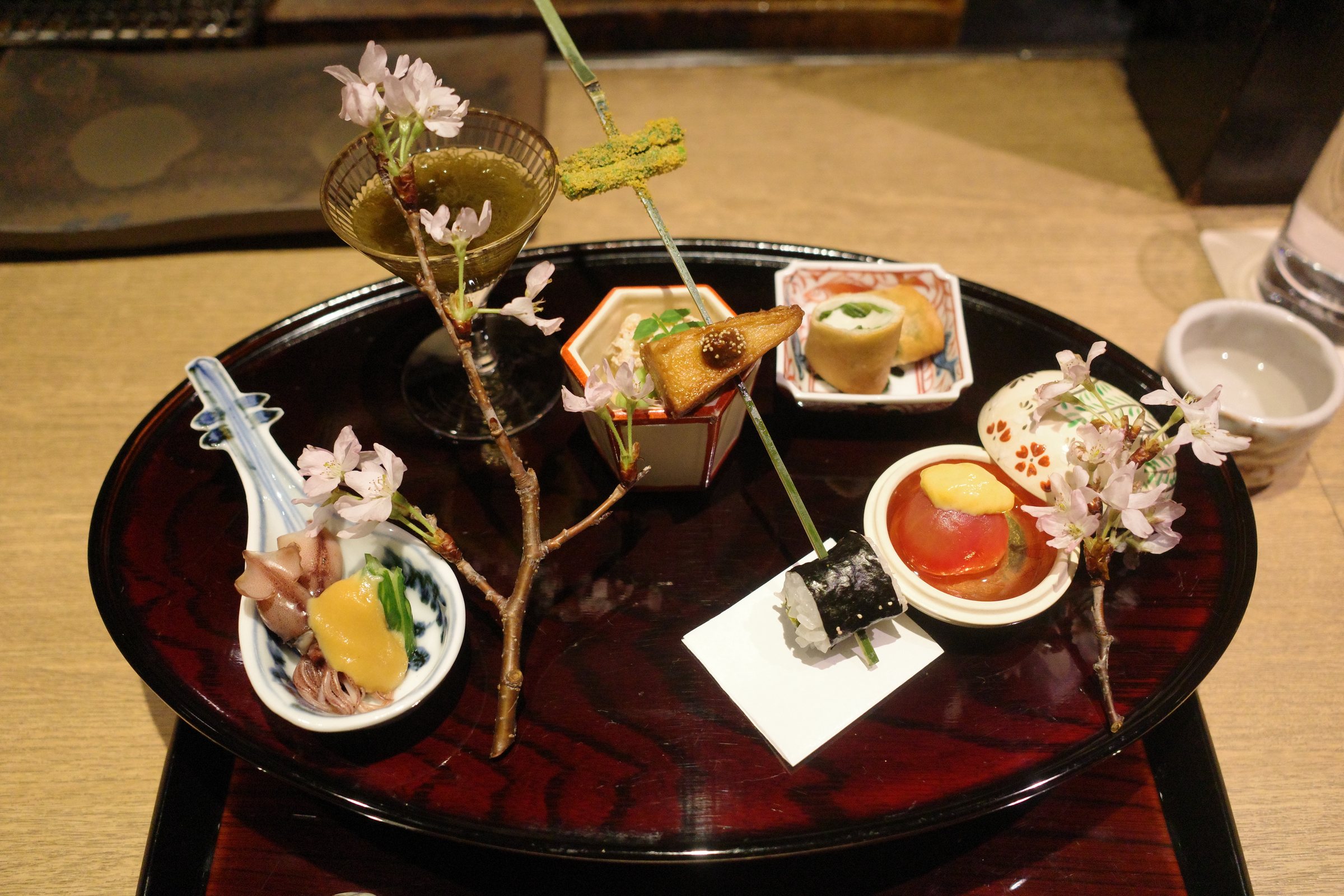 The spring hassun on a black lacquered tray, with cherry blossom, a skewer and small dishes.