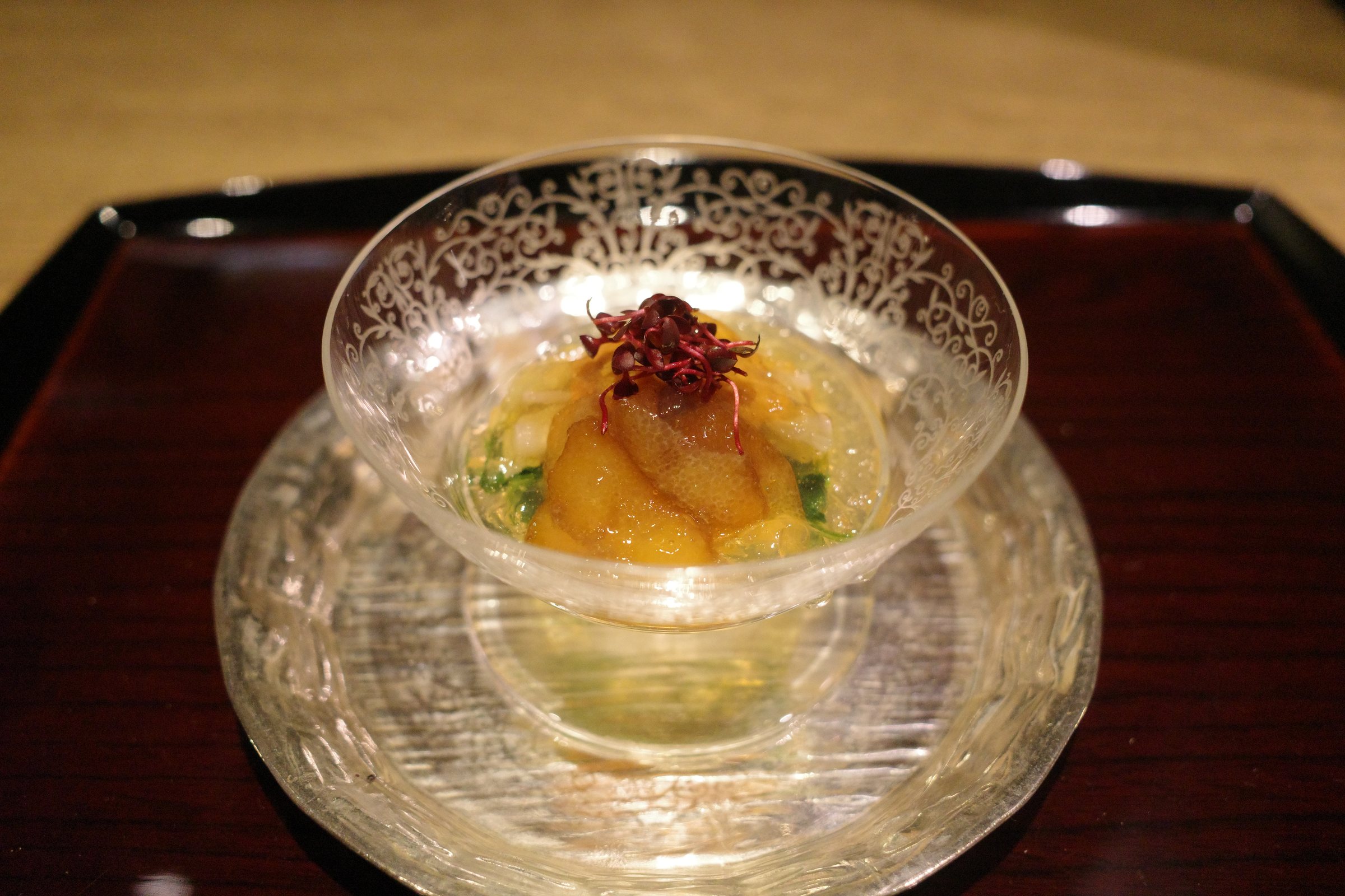 Herring roe, sea urchin and red tade sprouts set in jelly in a glass dish.