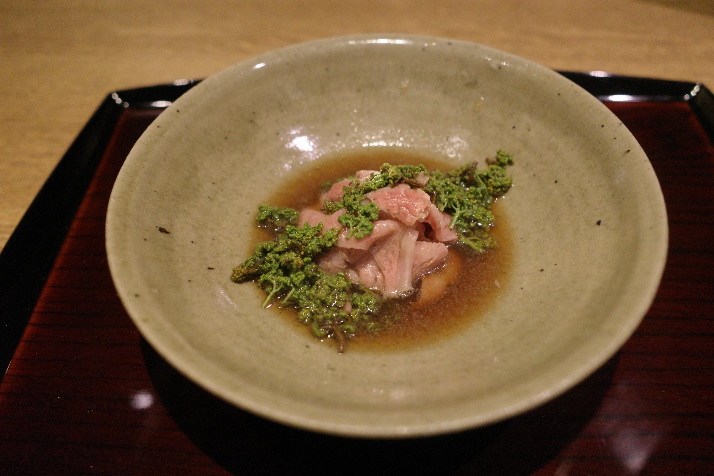 Thin slices of beef under a heap of flower sansho, in broth.