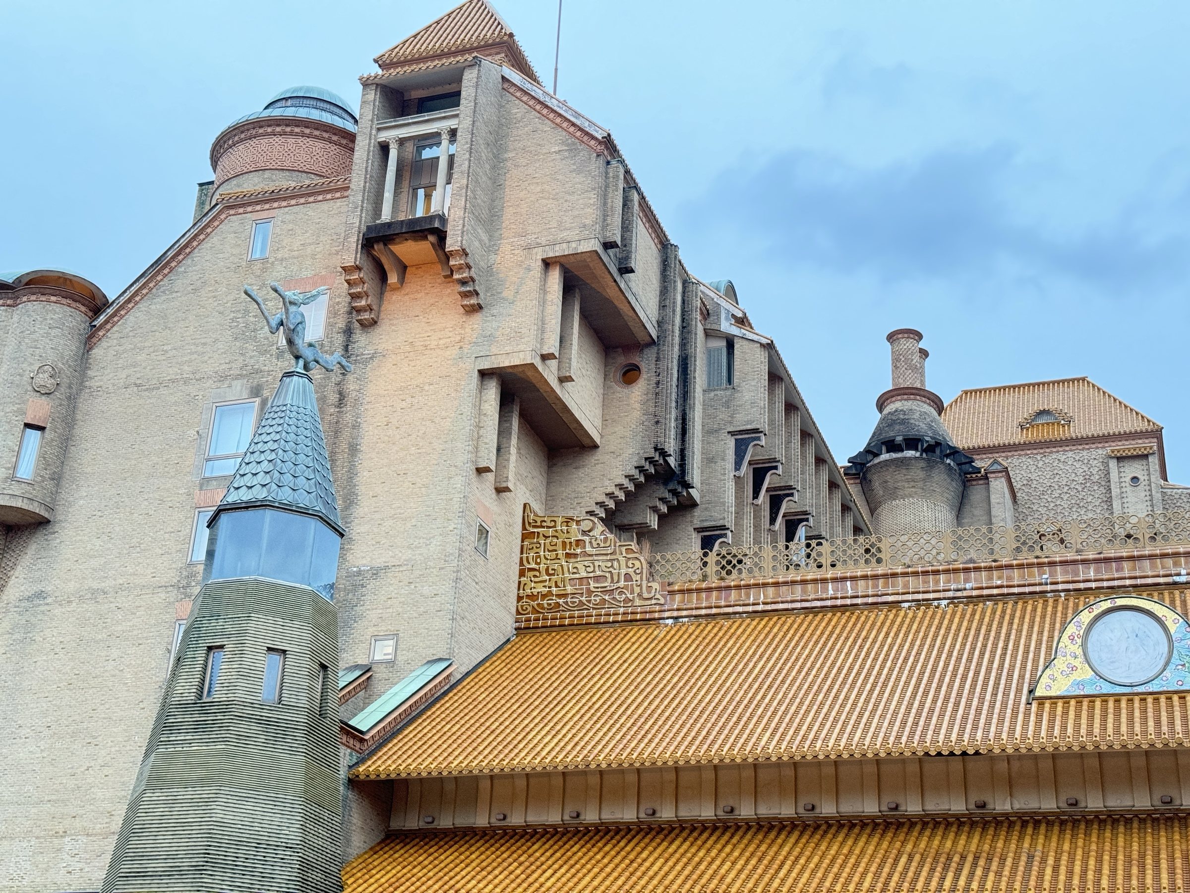 A spired turret with a rooftop sculpture rises above the tiled roof of the entrance.