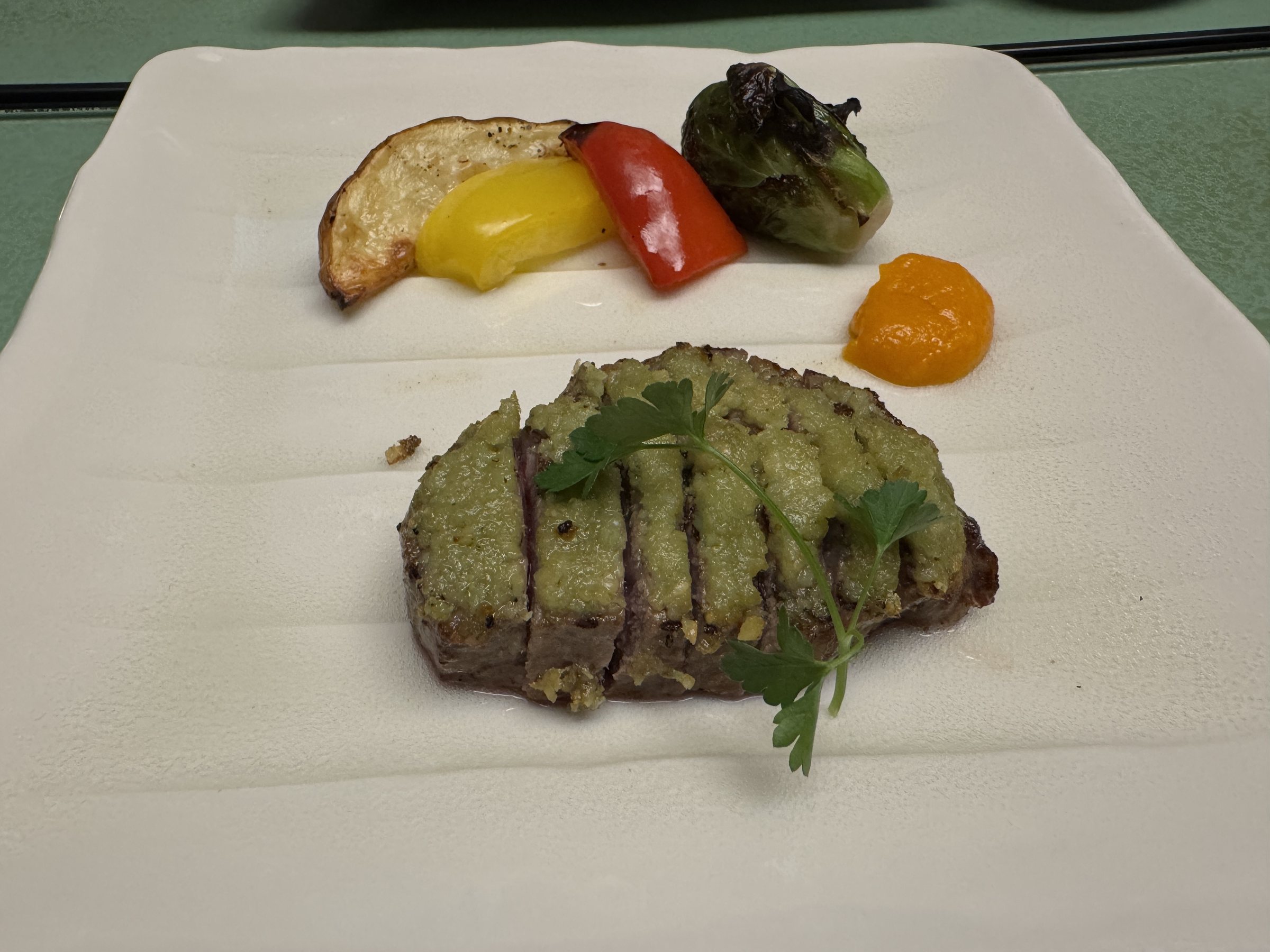 Grilled beef under a bright green topping, with roasted peppers.