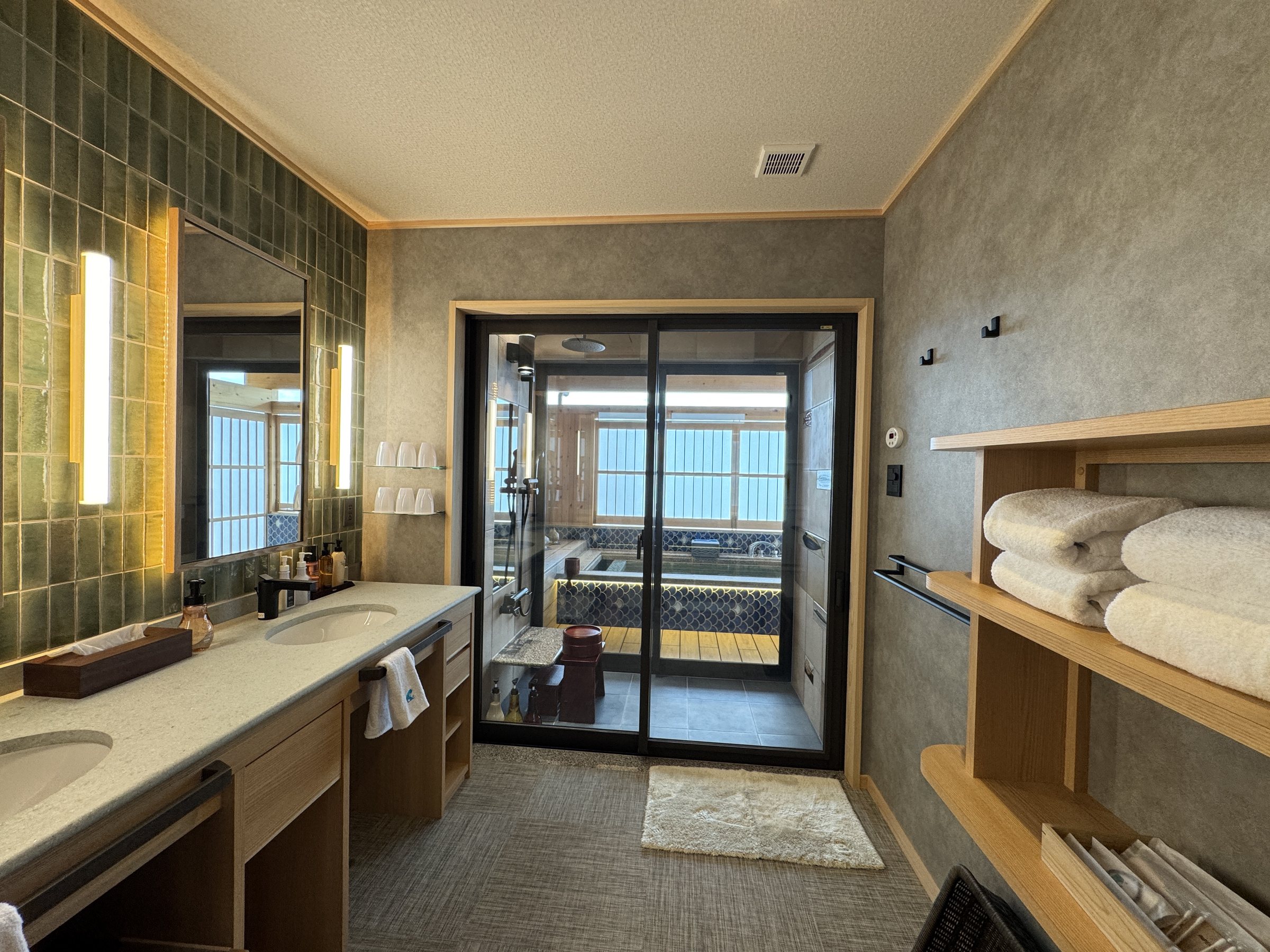 A double vanity with tiled walls, and the bath beyond the glass door.