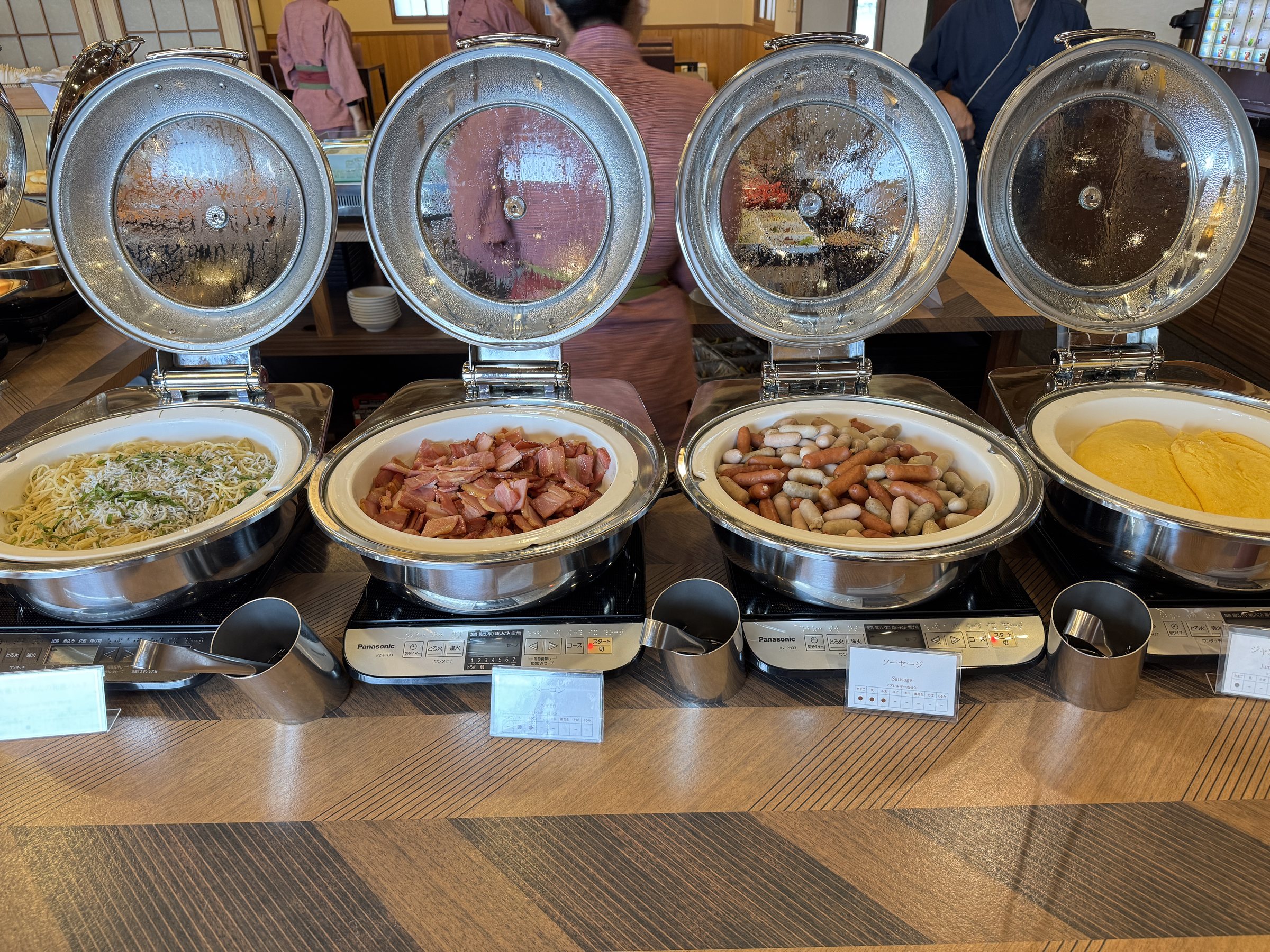 Pasta, sausages and scrambled eggs in chafing dishes.