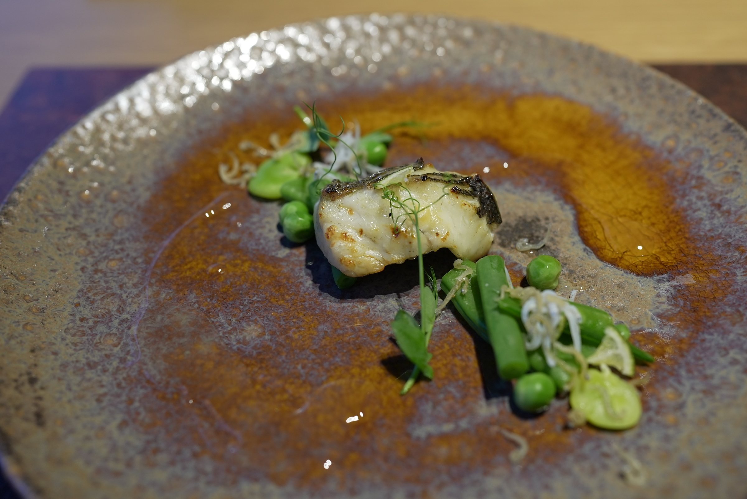 Wakasa-grilled sea bass with peas and beans in a pool of dashi.
