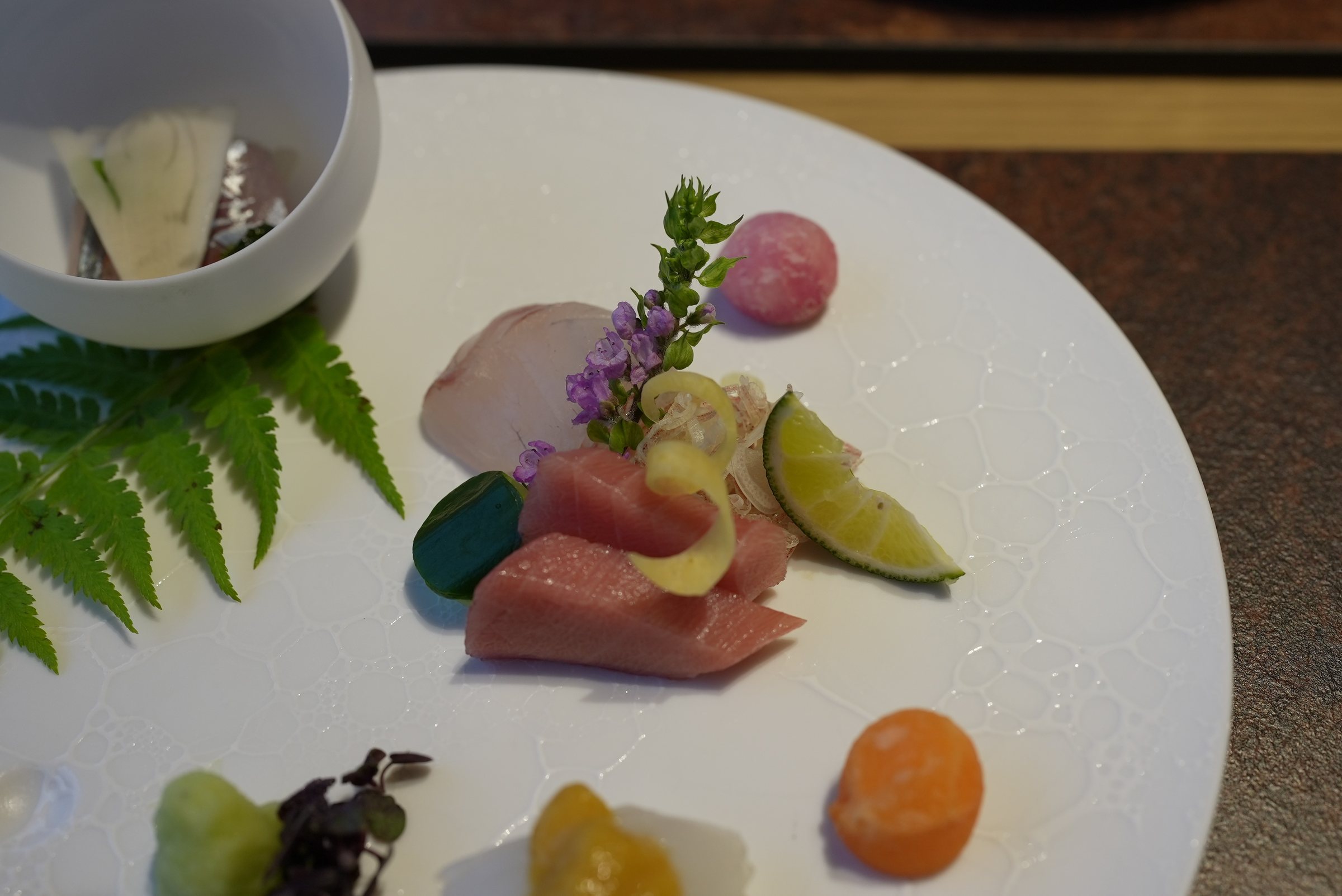 Seasonal sashimi on a white plate, dressed with fern and flowers.