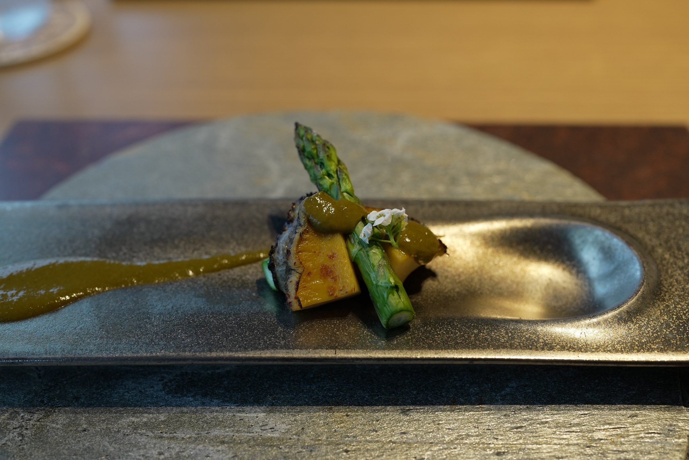 Charcoal-grilled abalone and green asparagus on a long metal plate.