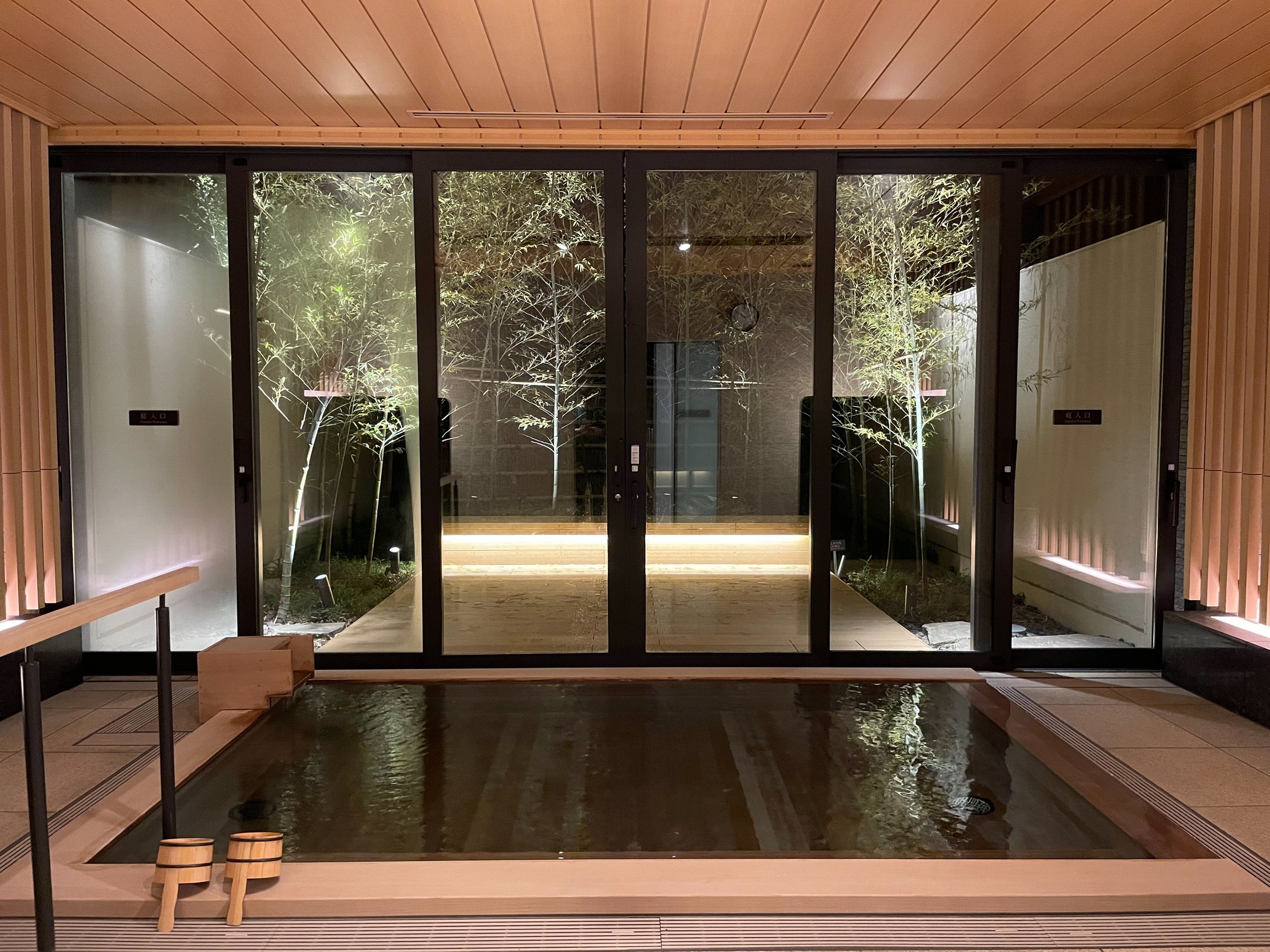 The hinoki tub, with lit bamboo beyond the glass.