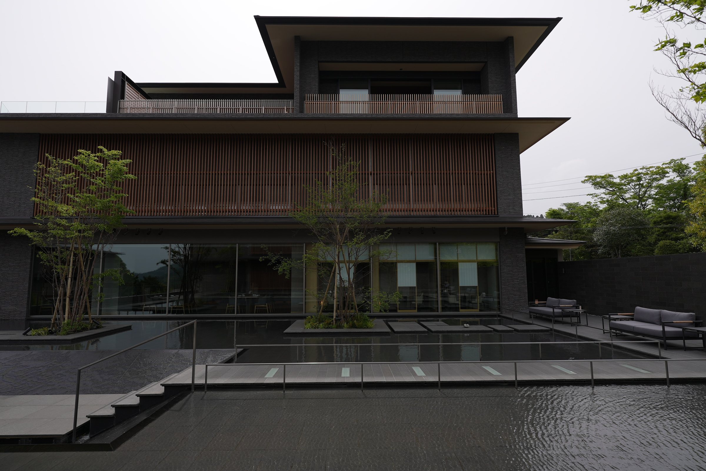 The water courtyard: still pools, stepping stones and timber-clad wings under a soft spring sky.