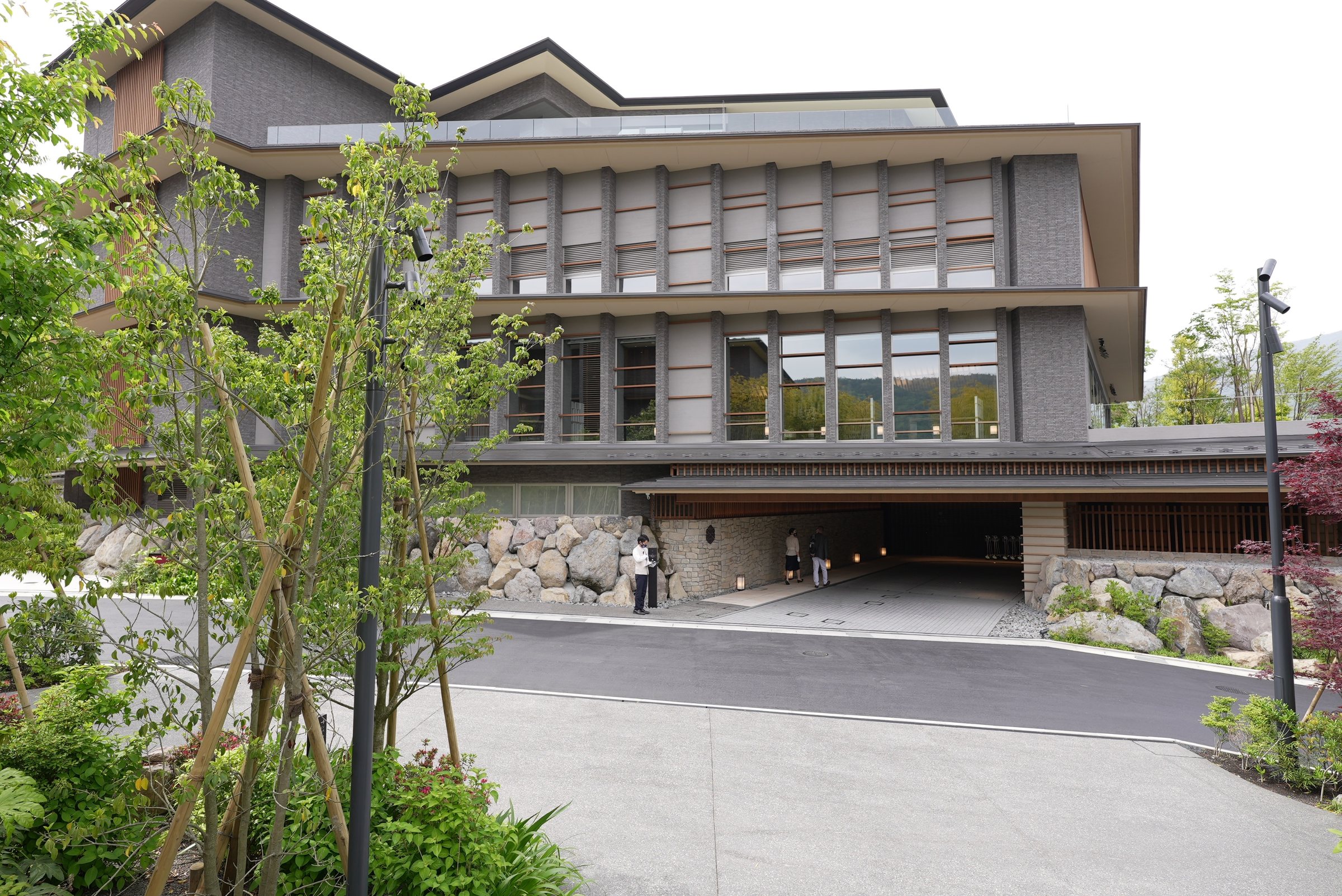 The forecourt: a low, layered building framed by young trees and mountain green.