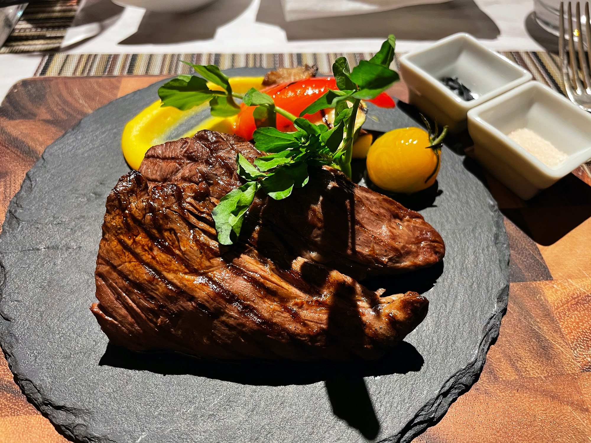 A thick, charred steak on a slate board, crowned with herbs.