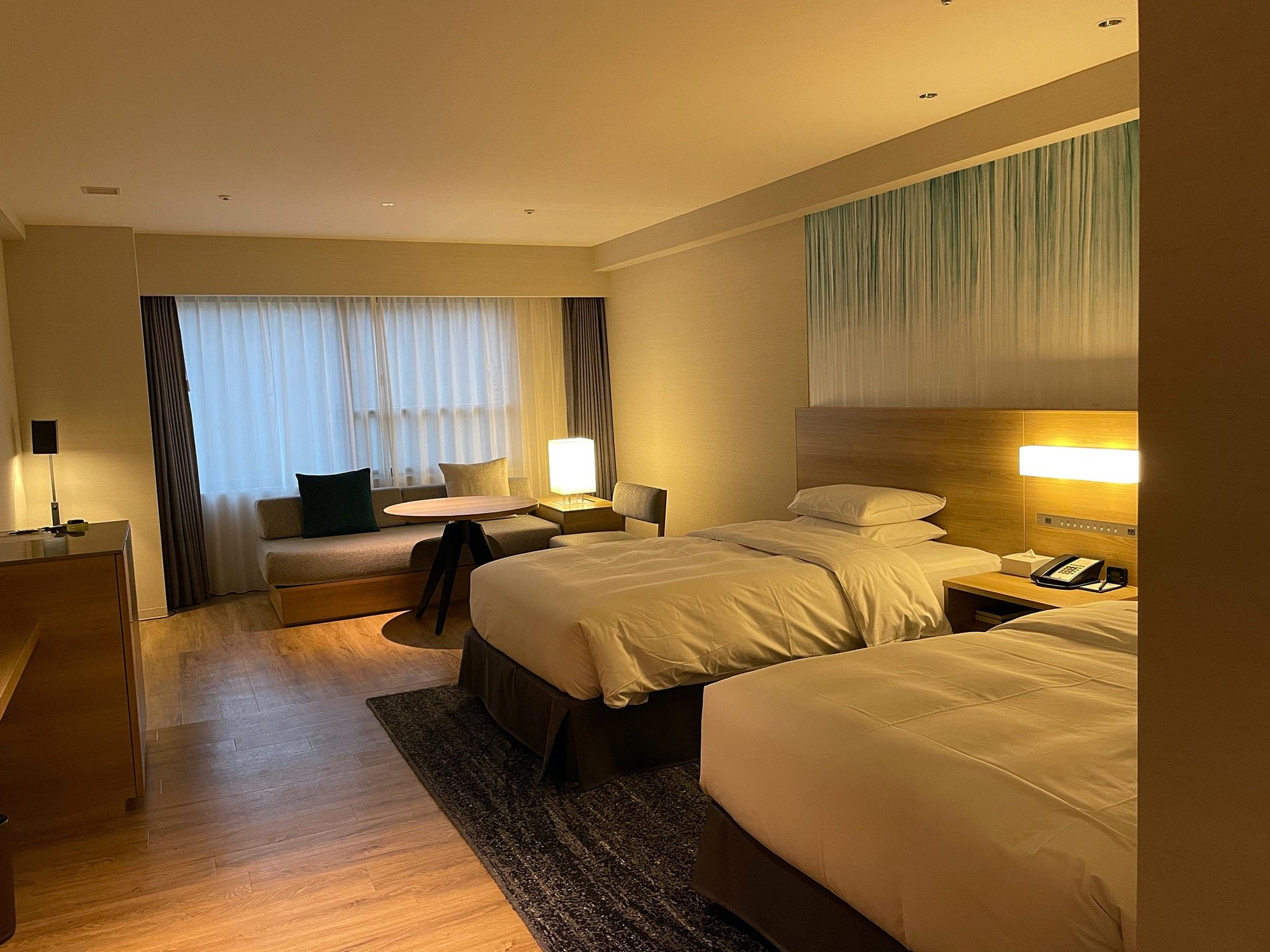 A clean, softly lit twin room with a sitting area by the window.