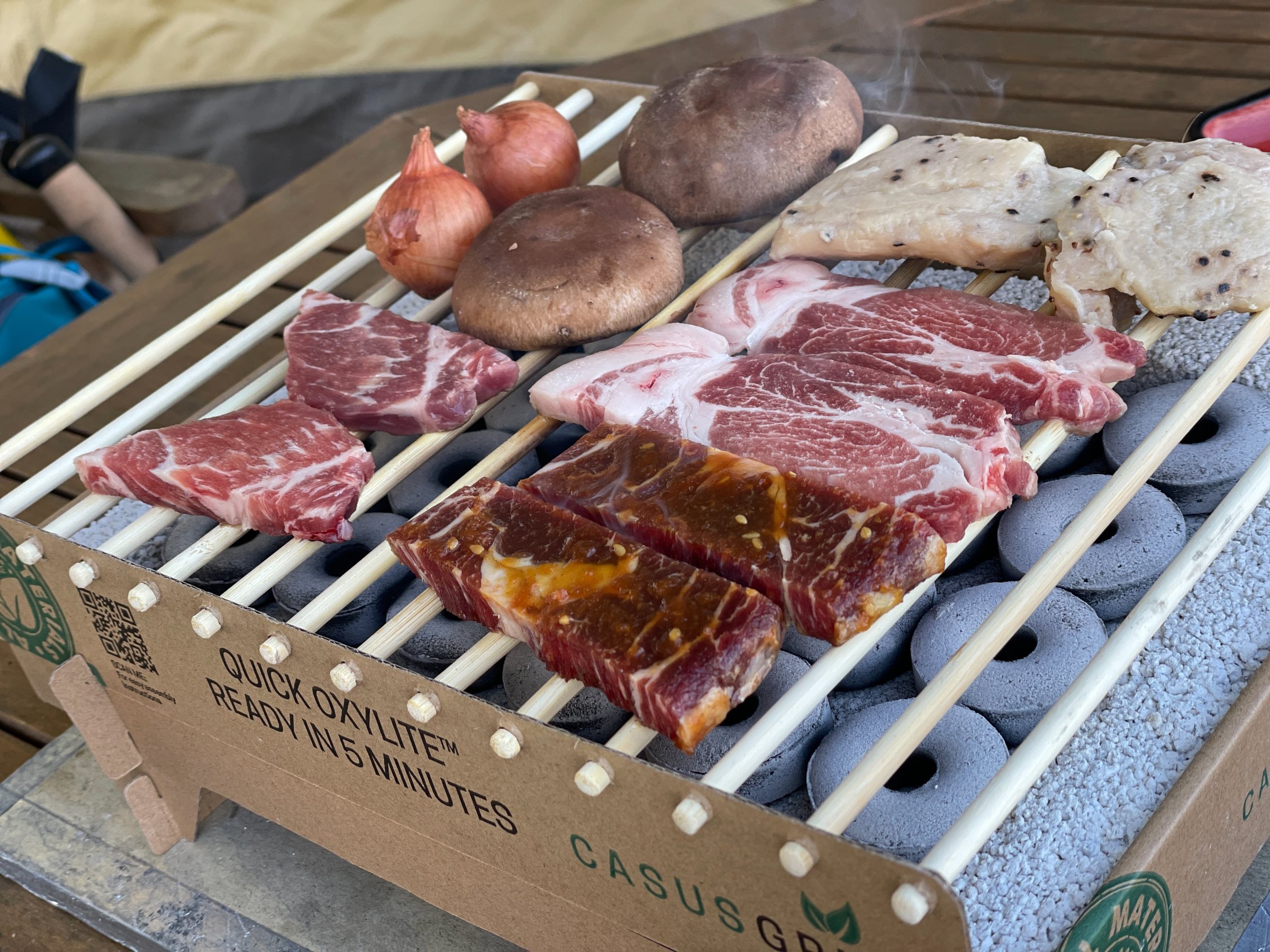 Beef, pork, onion and shiitake on the grill over cylindrical coals.
