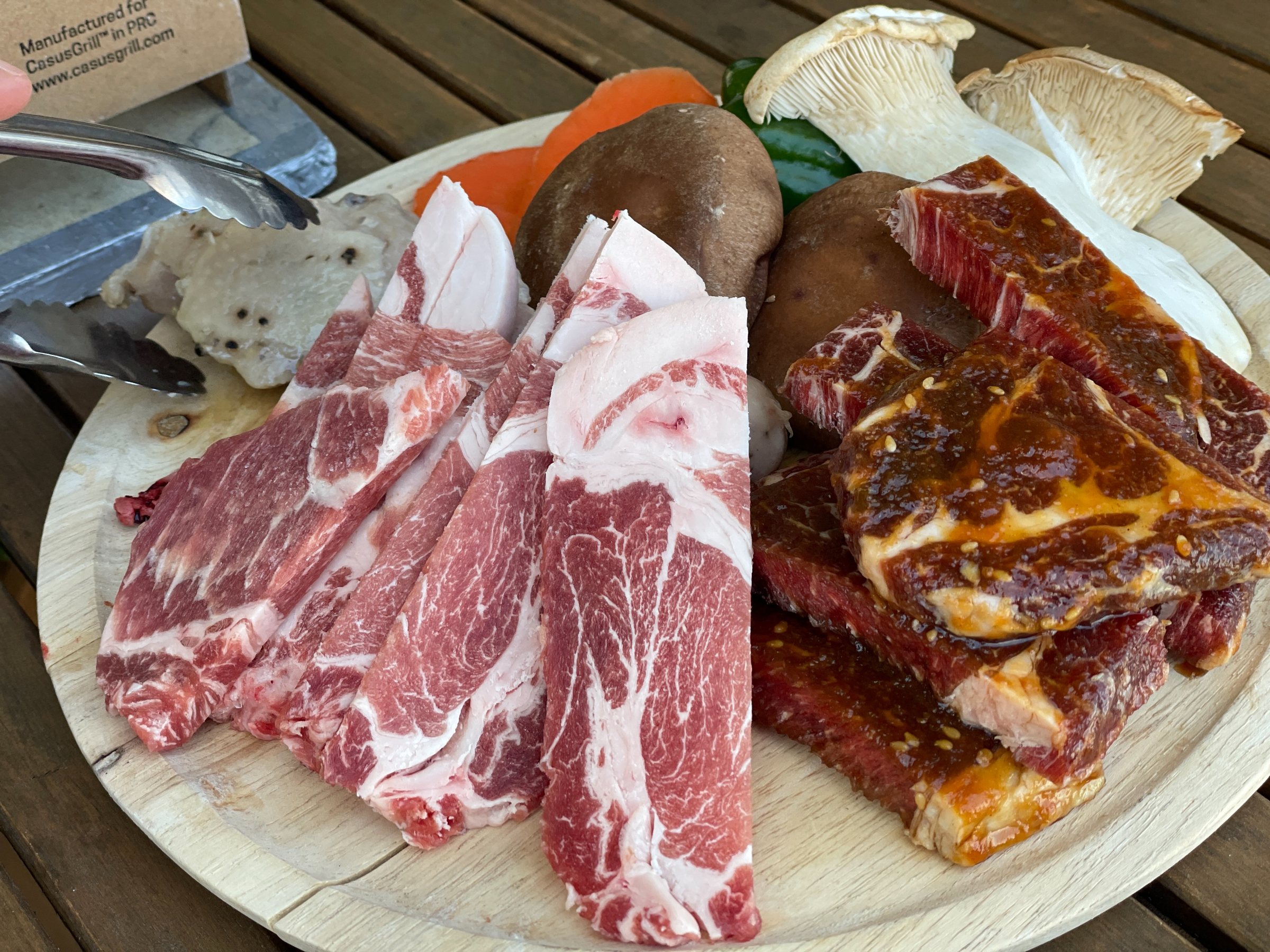 The platter: sliced pork, marinated beef, mushrooms and vegetables on a wooden board.