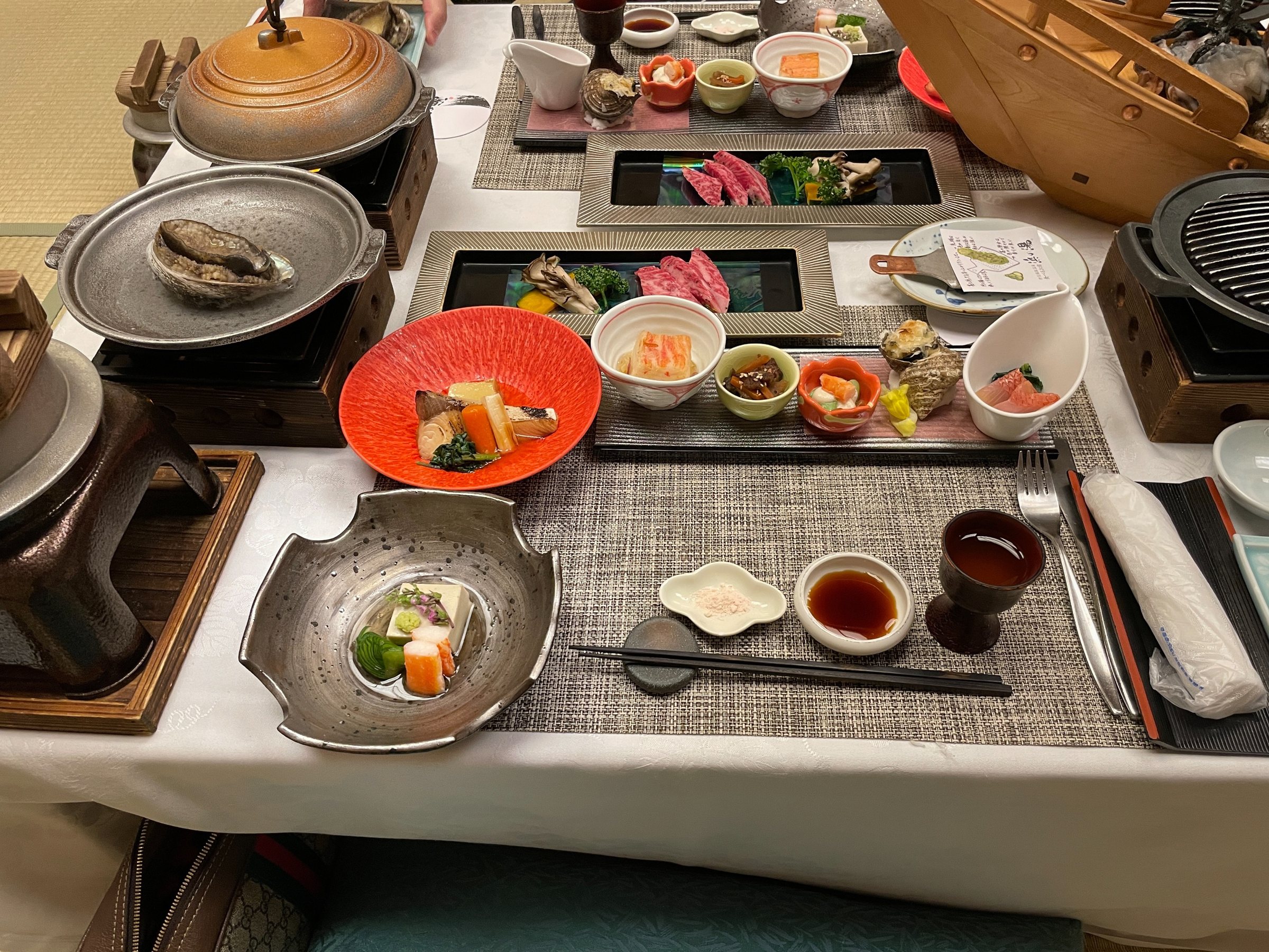 The dinner table: lacquered plates, hot stones, hot pots and a vermilion dish of small bites.