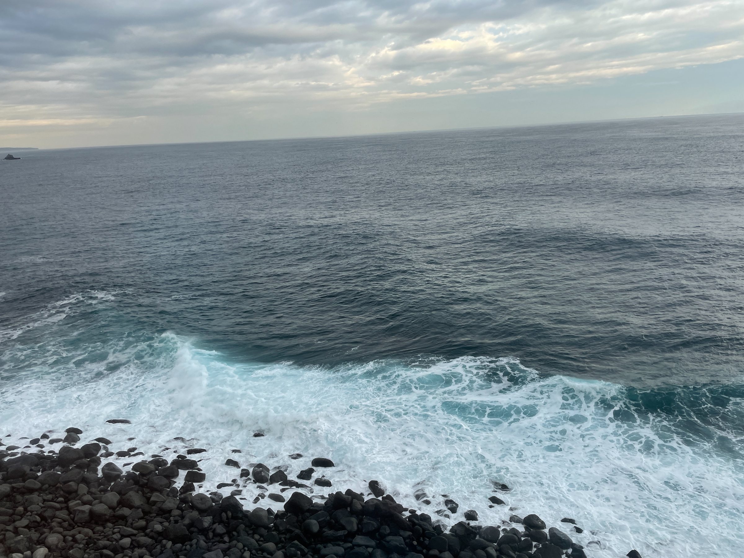 The open Pacific at Inatori: white water breaking over a black stone shore.