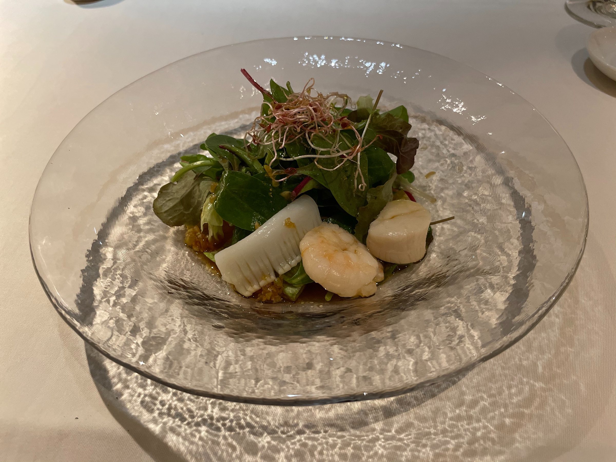 A composed salad of greens and seafood on a glass plate.