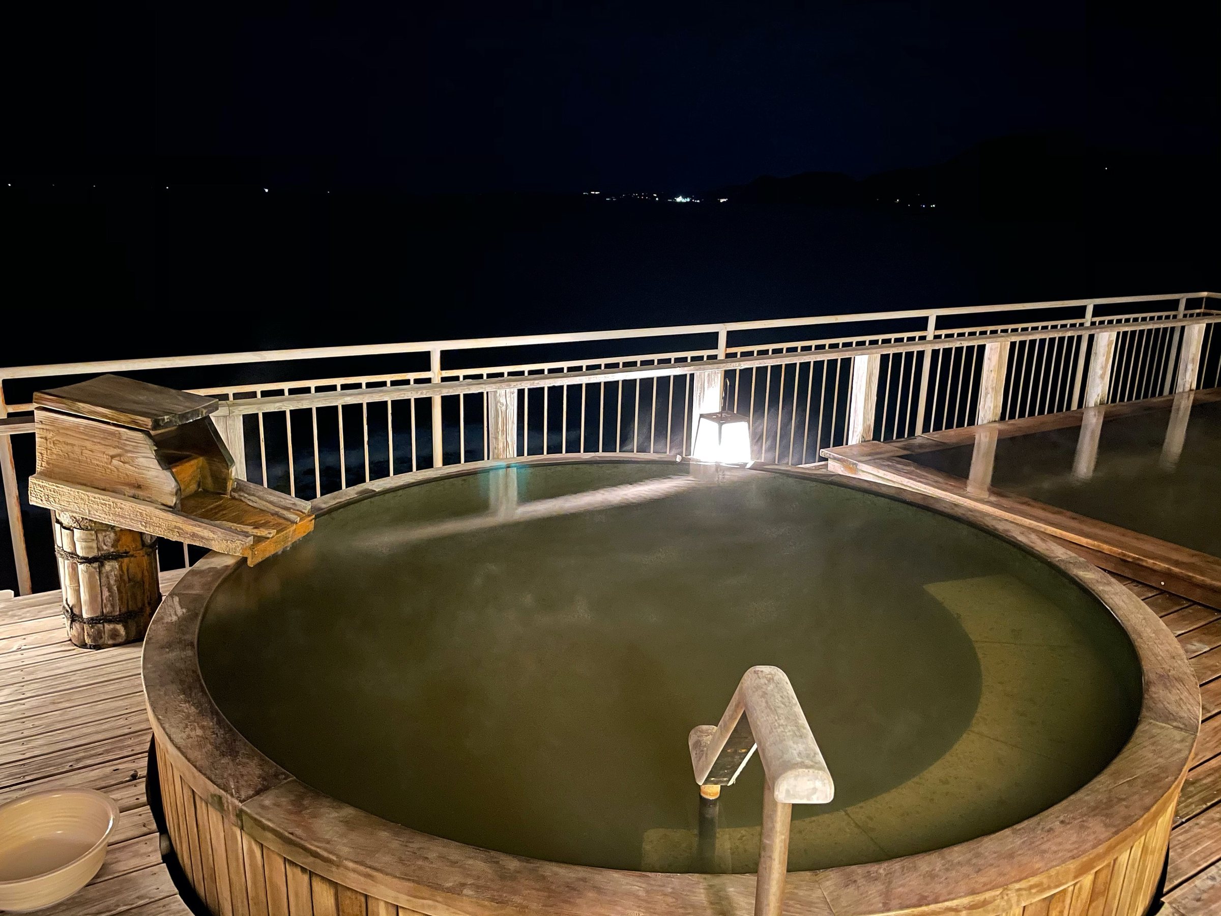 The round rooftop bath at night, the sea dark beyond the rail.