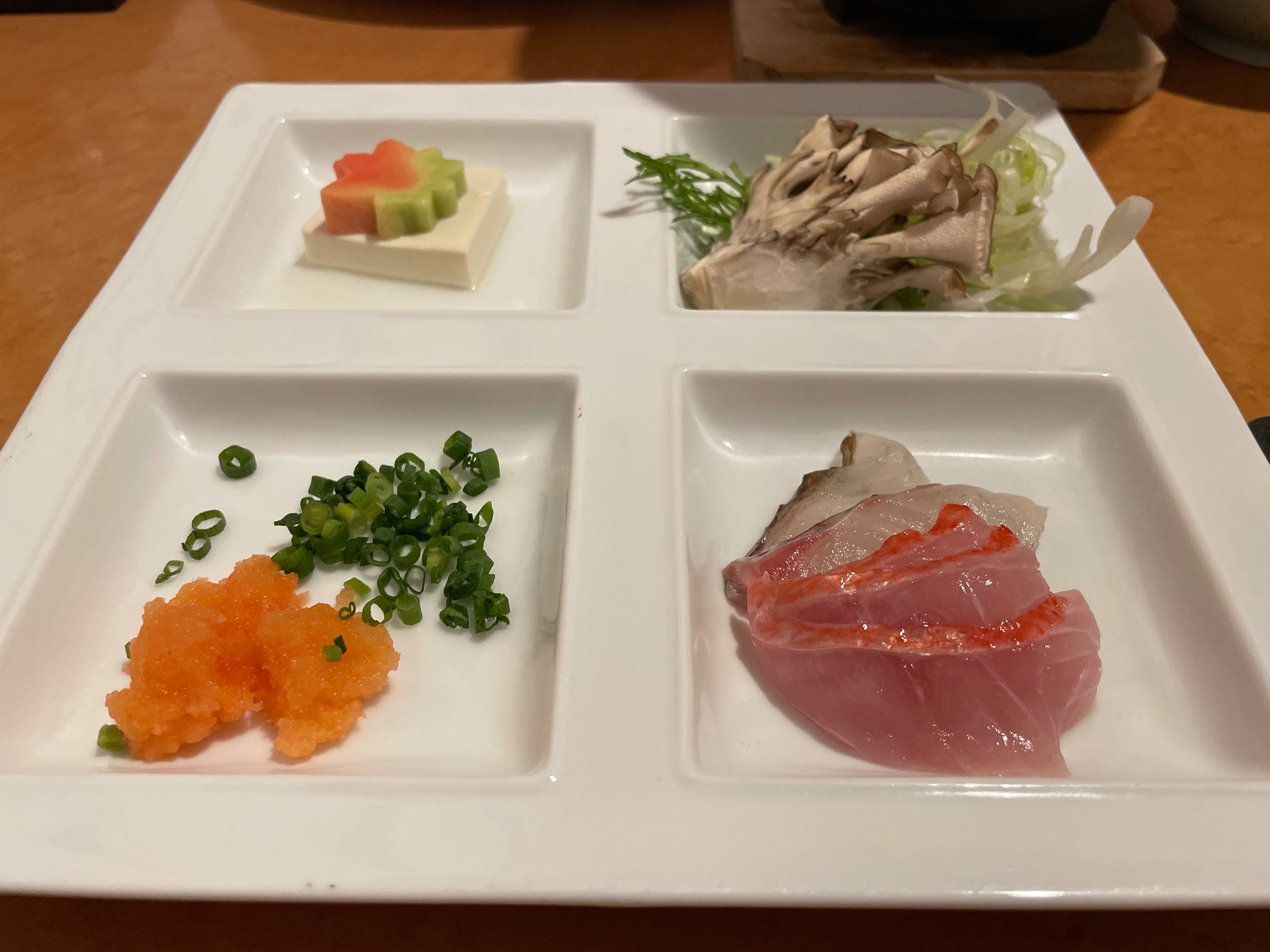 A four-part plate of small bites and sashimi.