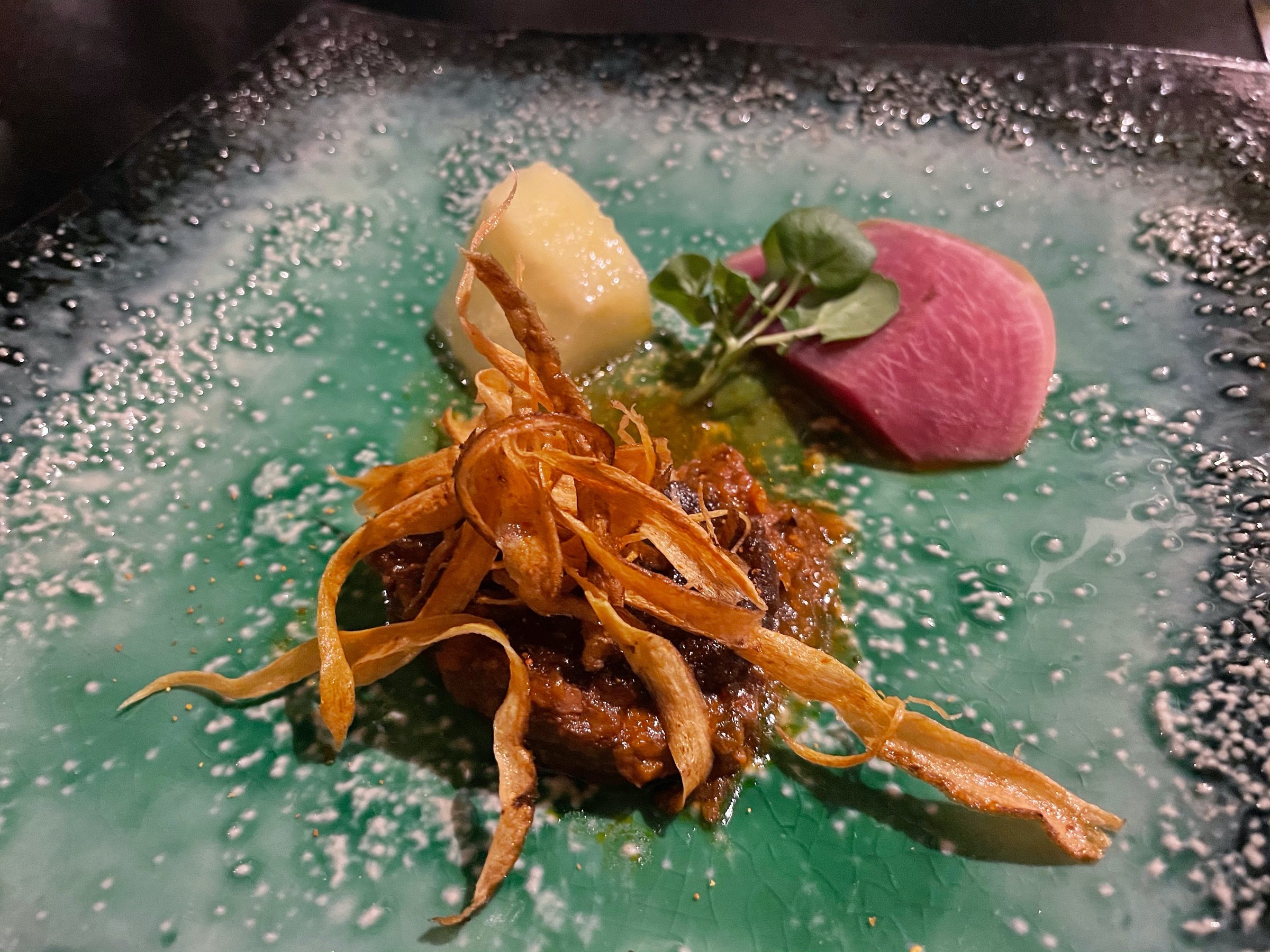 The meat course, topped with crisp fried ribbons, on a green-glazed plate.
