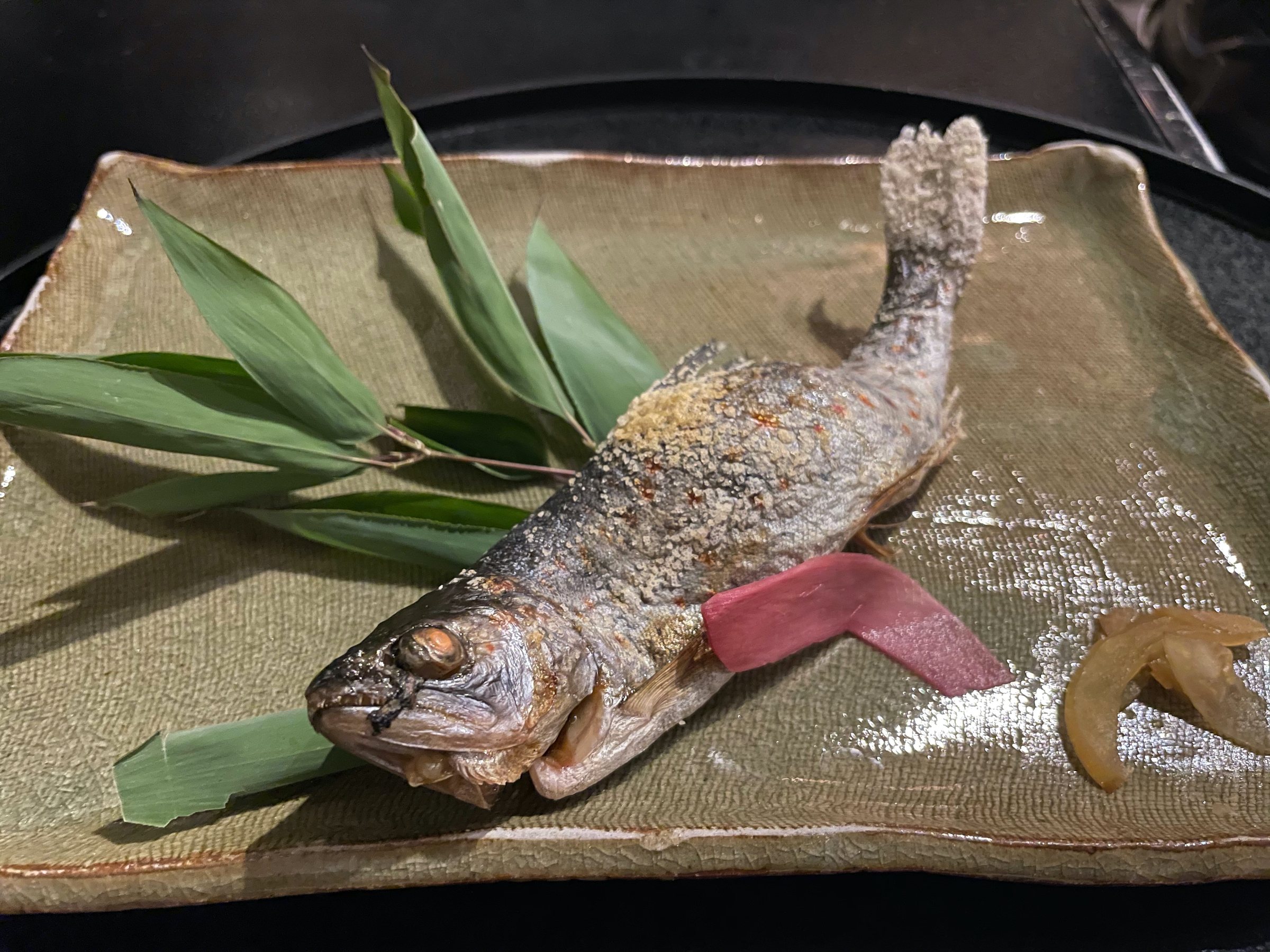 A whole grilled river fish laid on bamboo leaves.