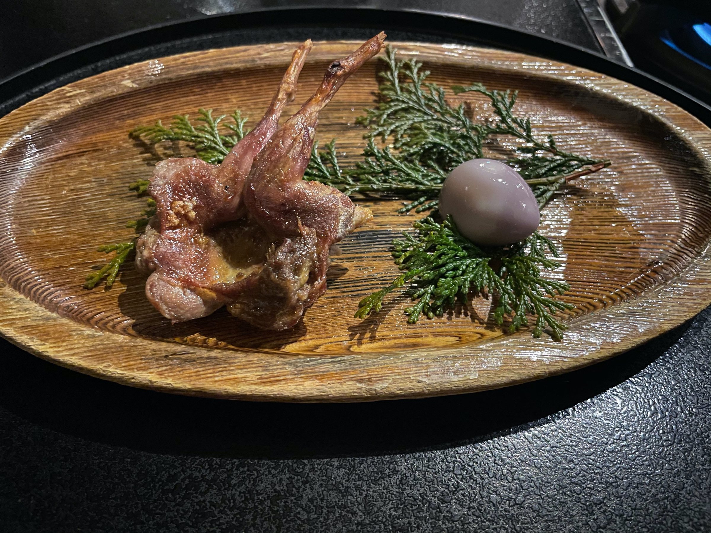 Grilled quail, with a speckled egg and sprigs of cedar.