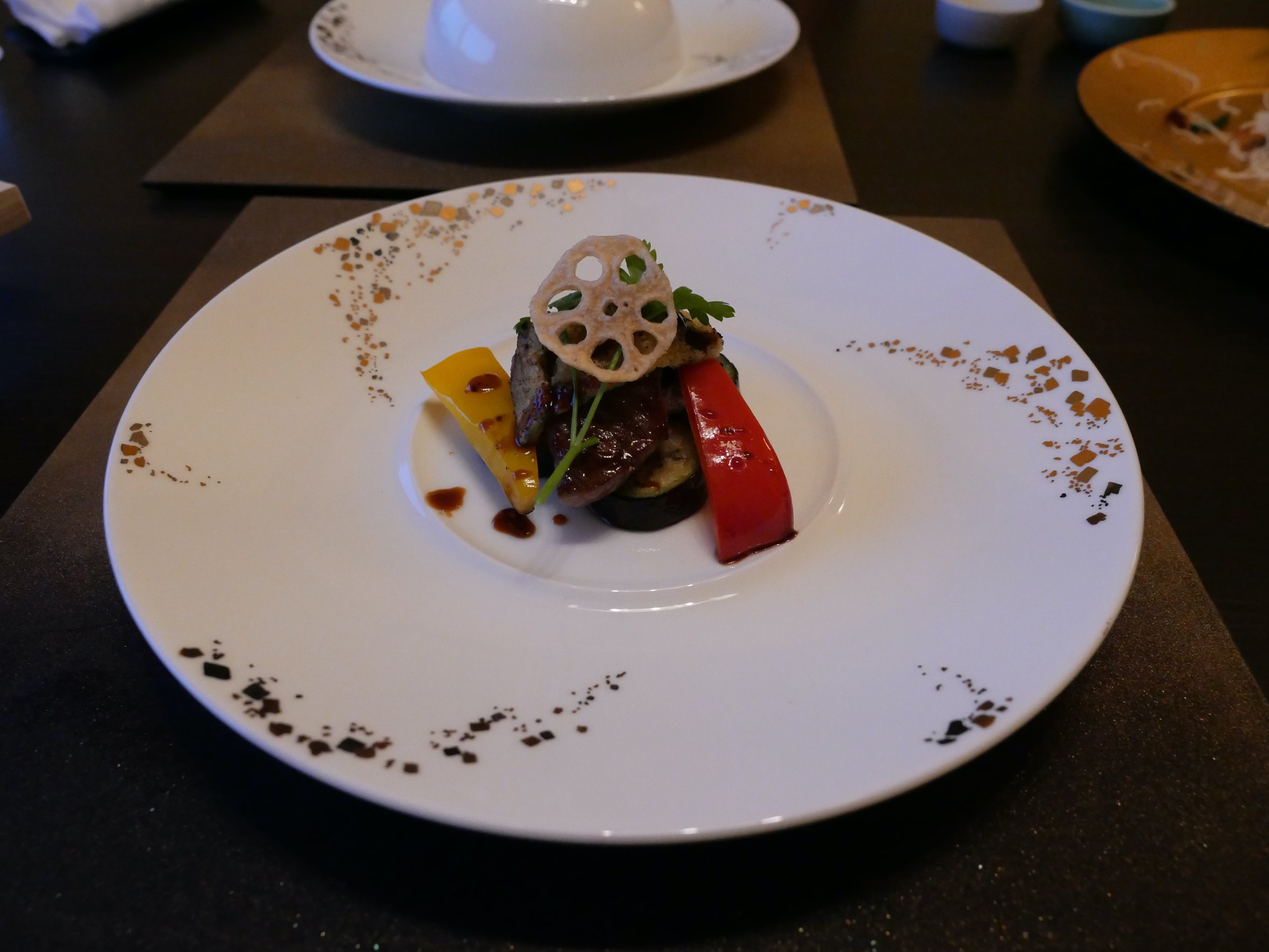 The meat course, stacked with grilled vegetables and a slice of lotus root.