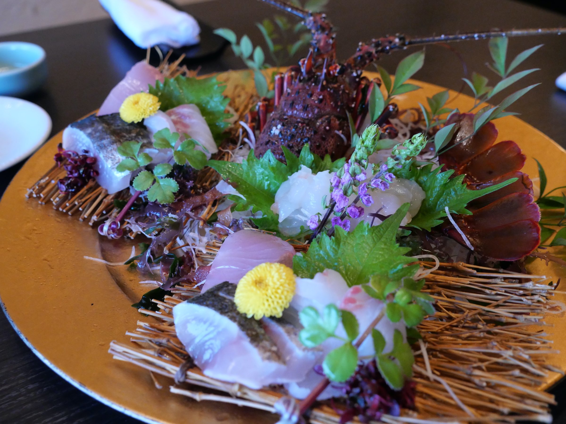 The sashimi platter: lobster head, seared fish and flowers on a bed of twigs.