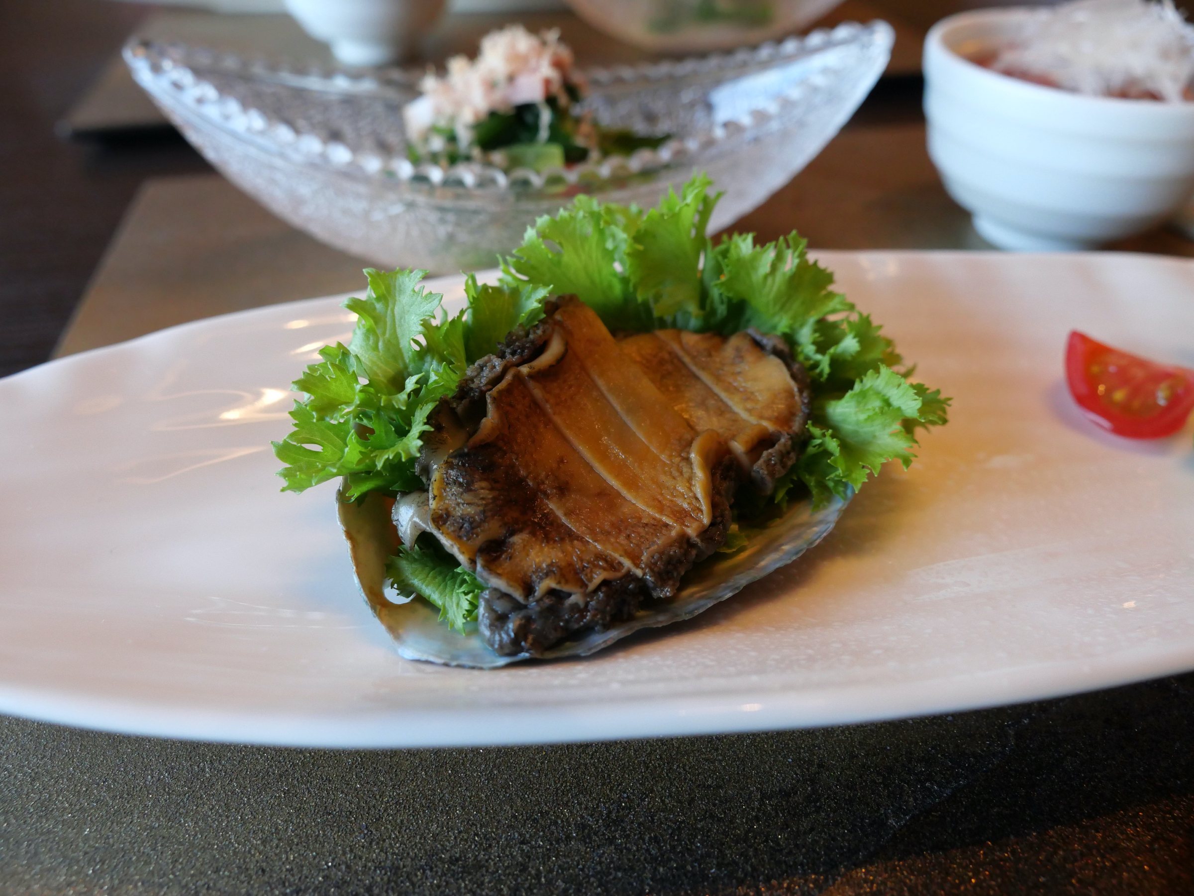 Abalone in its shell on a bed of lettuce.