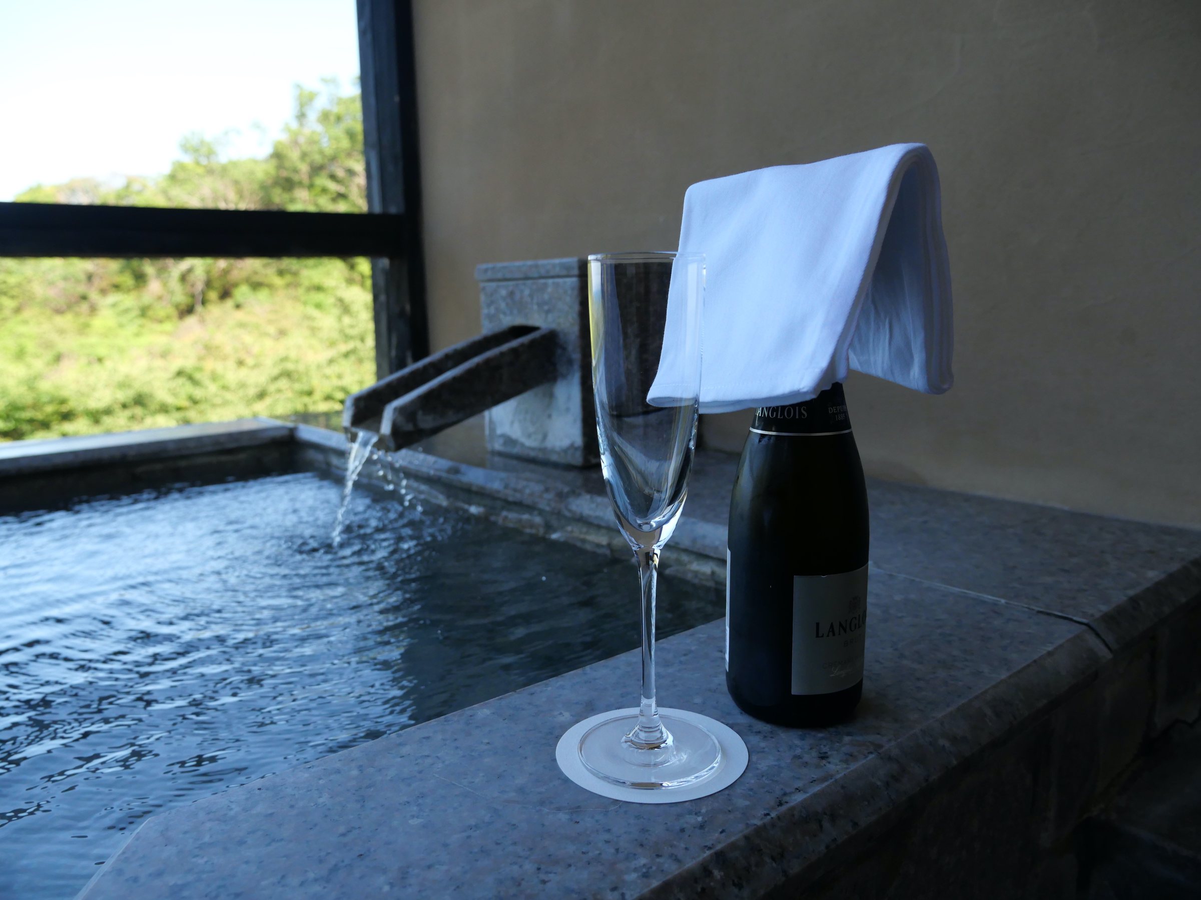 The open-air bath, with a glass and a bottle of sparkling wine on its edge.